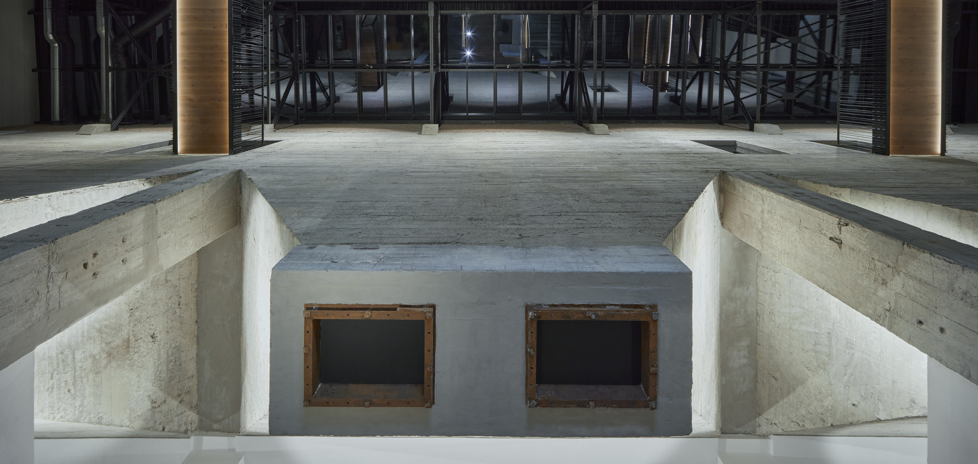 Sunken concrete volume with two timber-framed openings beneath an exposed structural ceiling