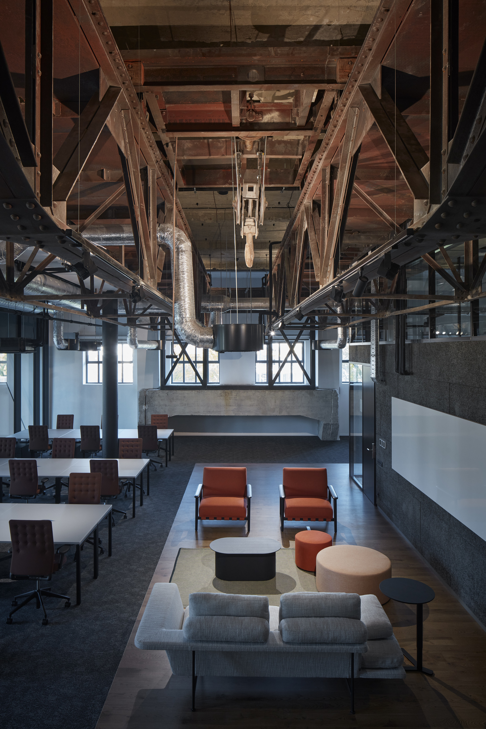 Double-height space with exposed timber trusses and steel bracing framing the seating area below