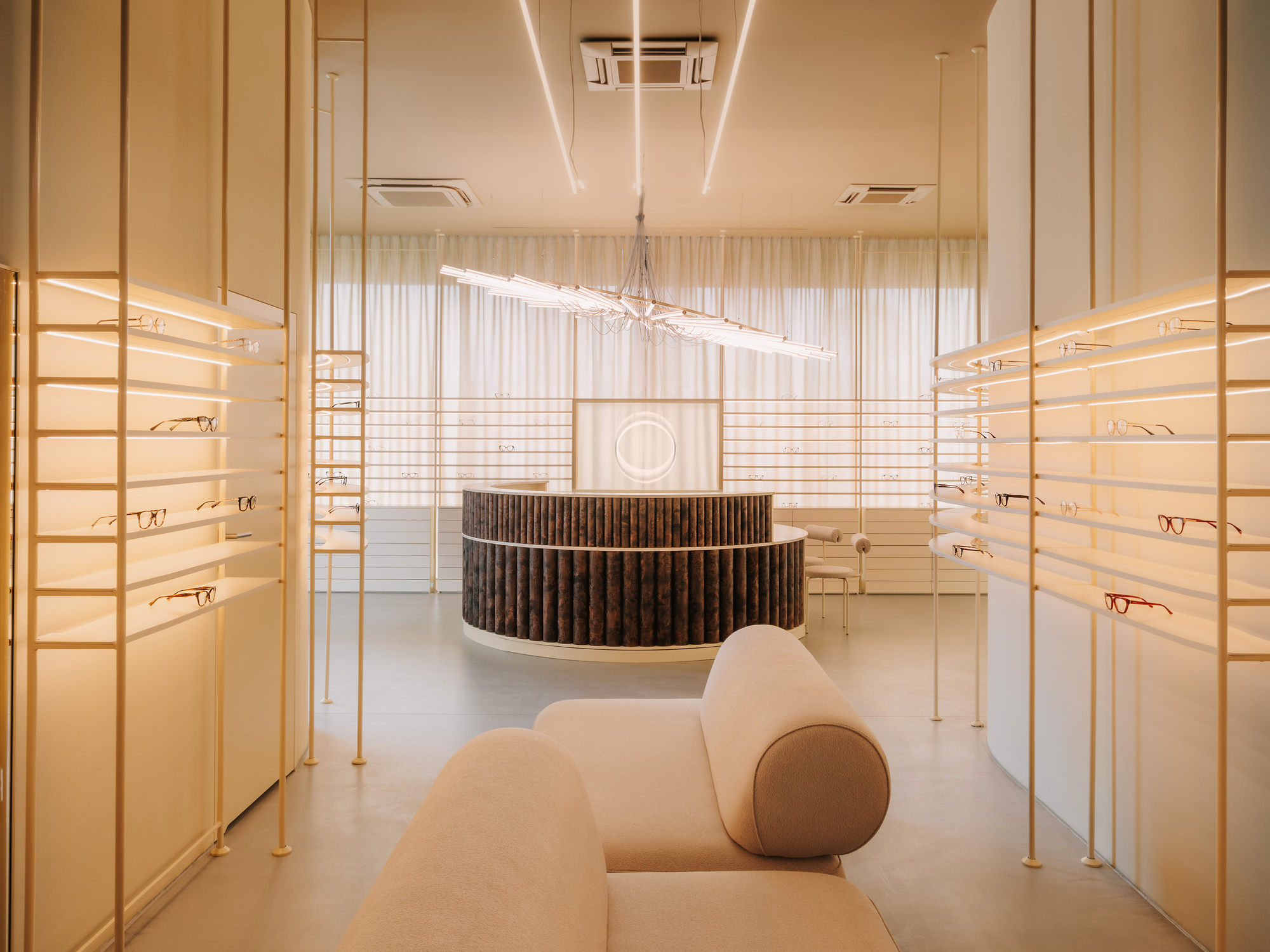 Interior view of an optical shop with backlit display shelves flanking a curved reception desk and linear ceiling fixture