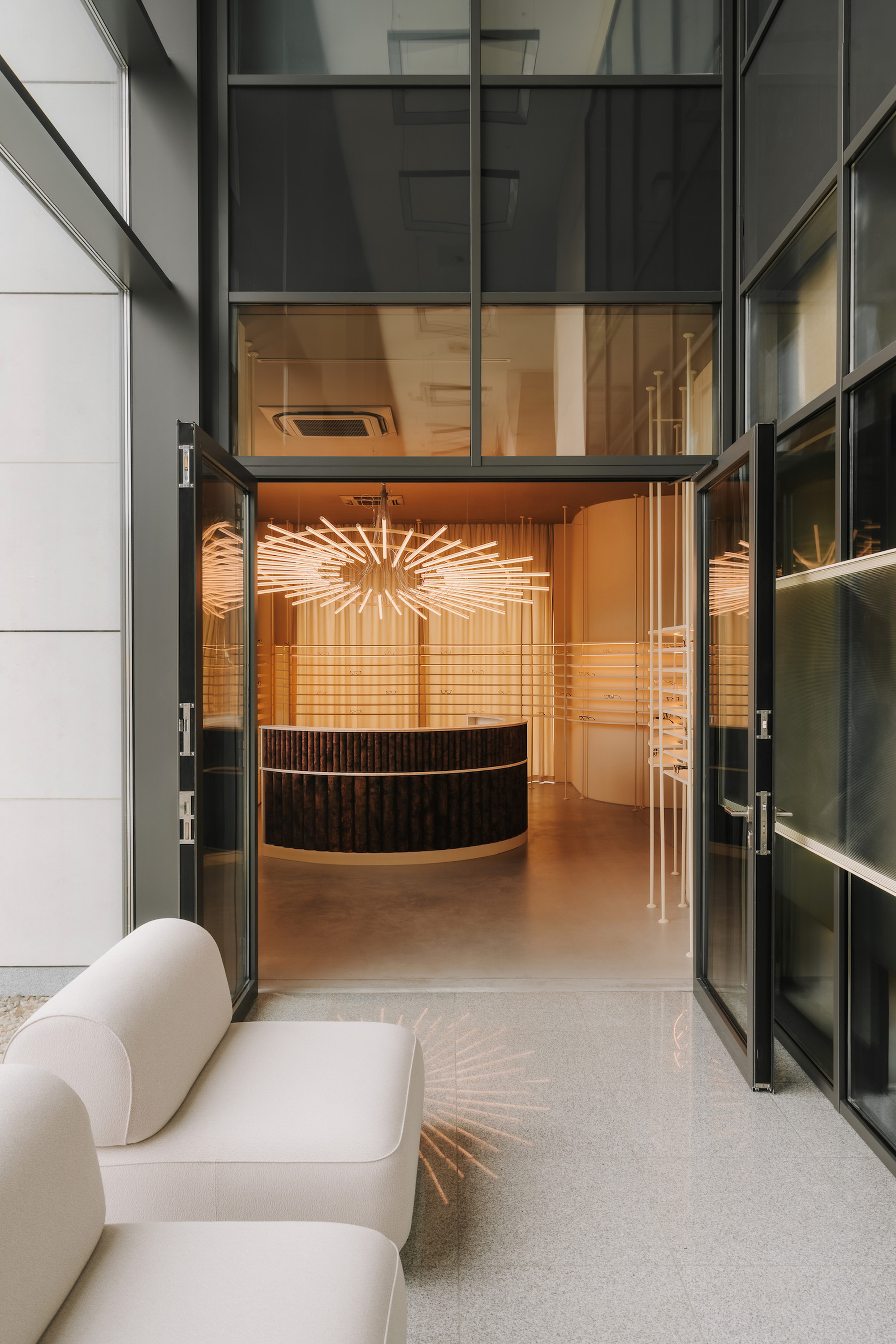 Entrance view through a steel-framed glass door into the retail space with eyewear displays and sculptural seating