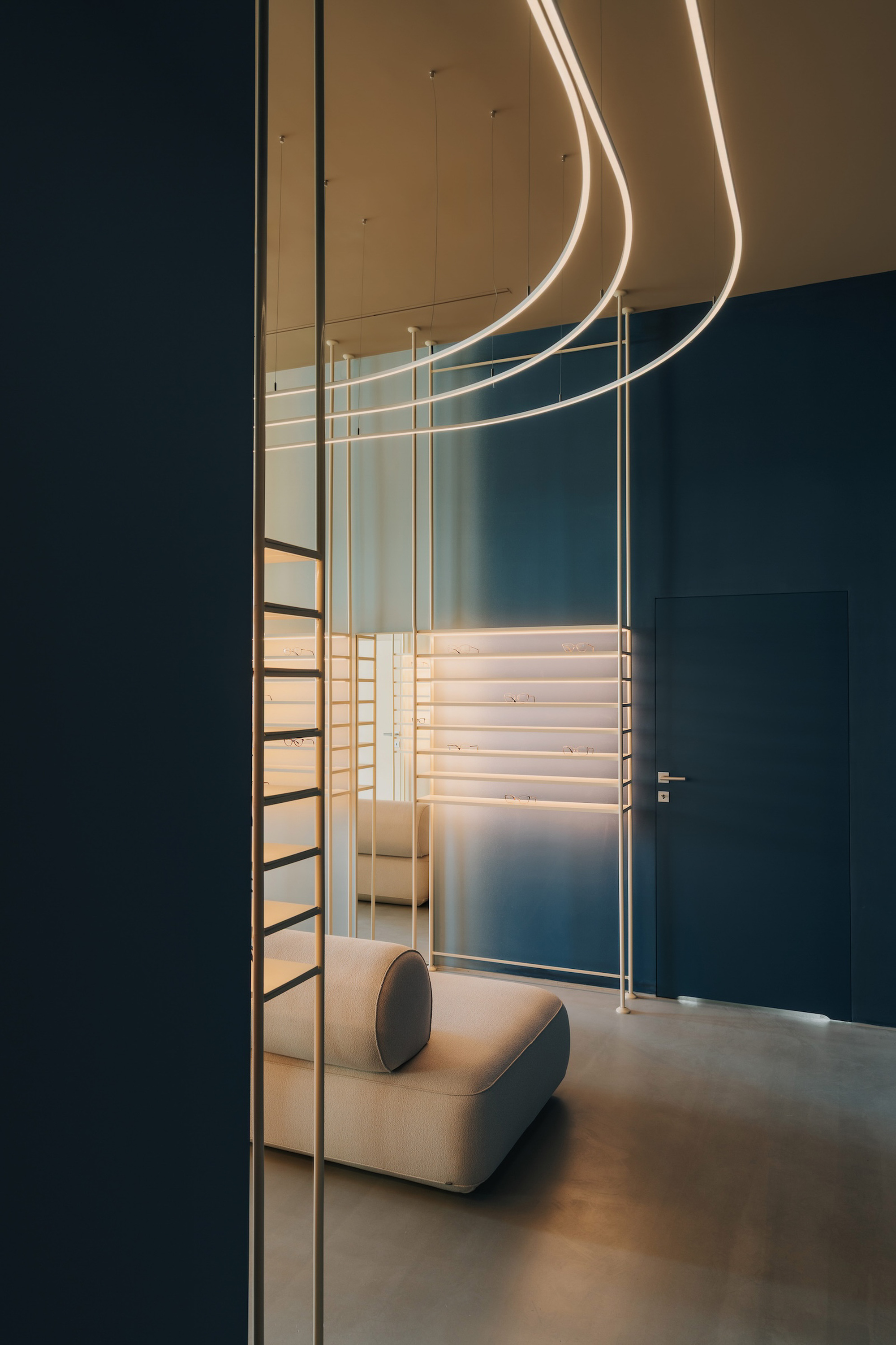Close-up of backlit display shelving with brass rods and curving light tubes against a dark teal partition wall