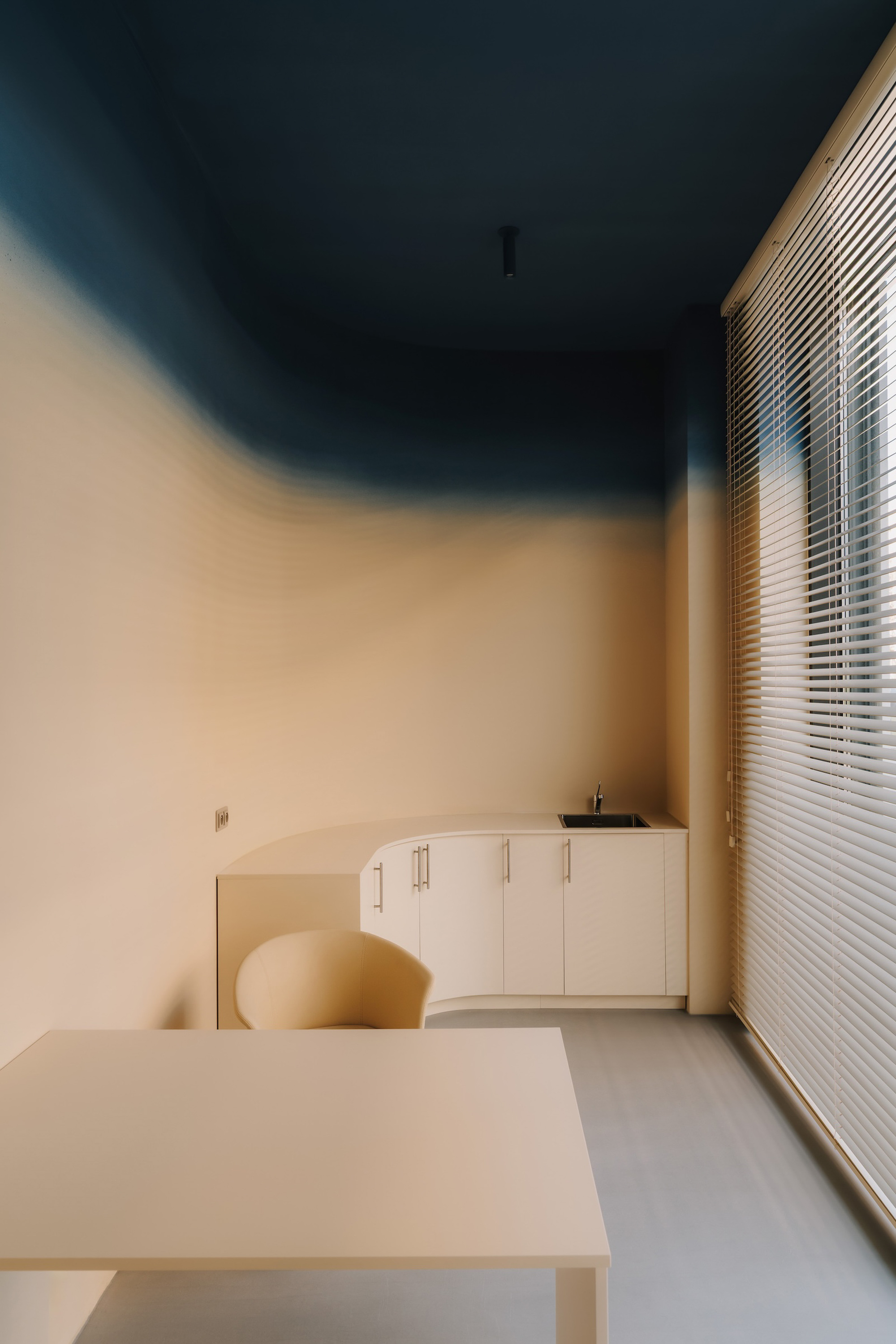 Workroom with pale cabinetry beneath a teal ceiling and horizontal blinds filtering daylight