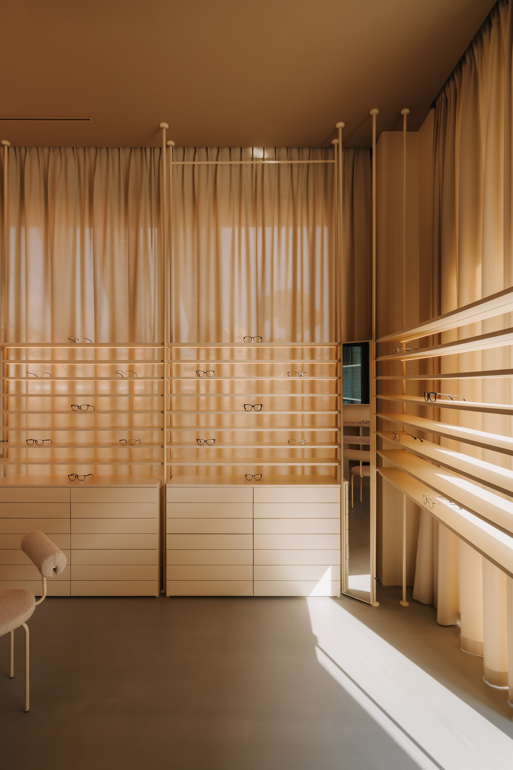 Eyewear display shelving with floor-to-ceiling sheer curtains filtering warm afternoon light