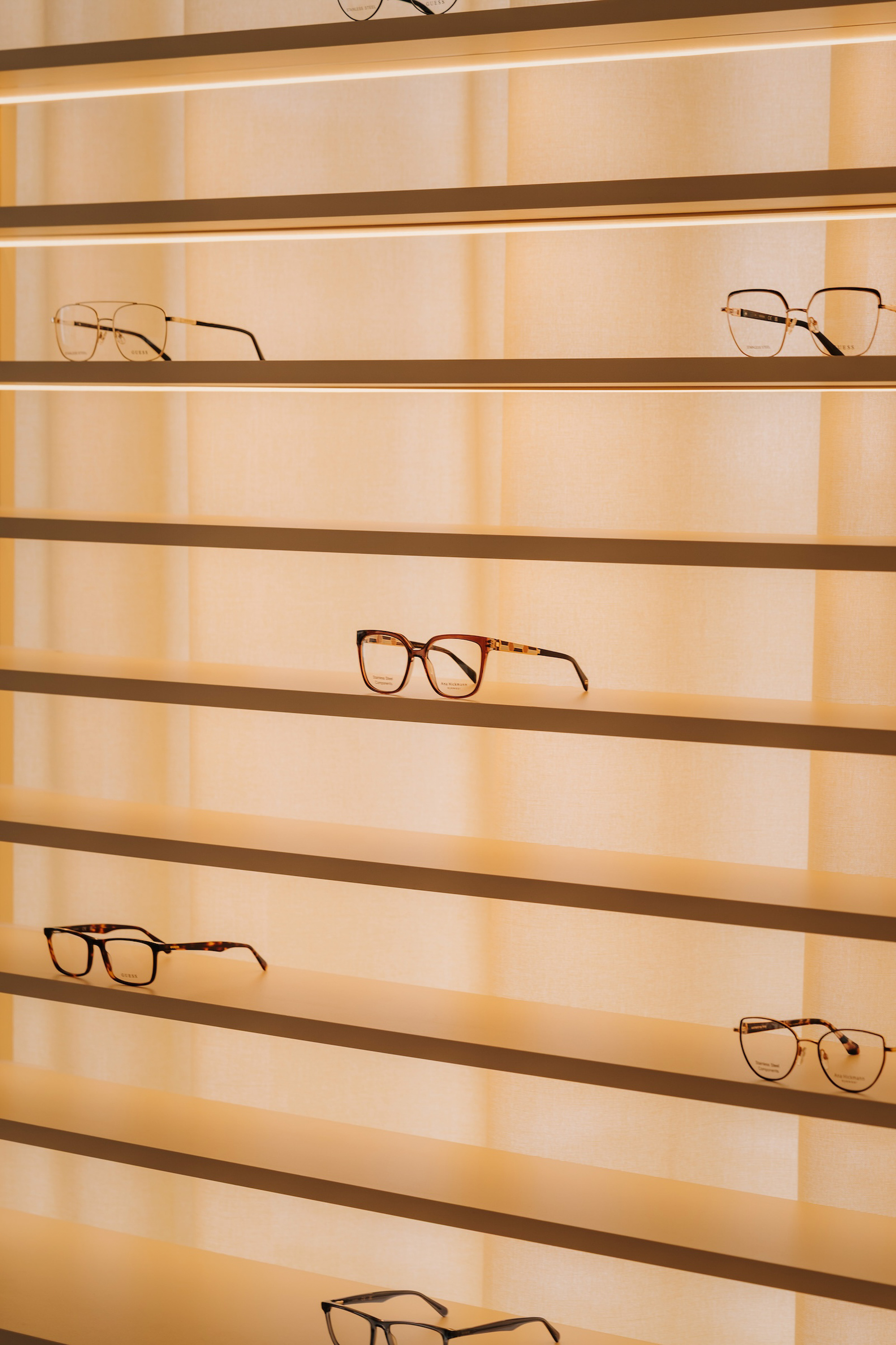 Backlit horizontal brass shelving displaying eyeglasses against translucent vertical panels