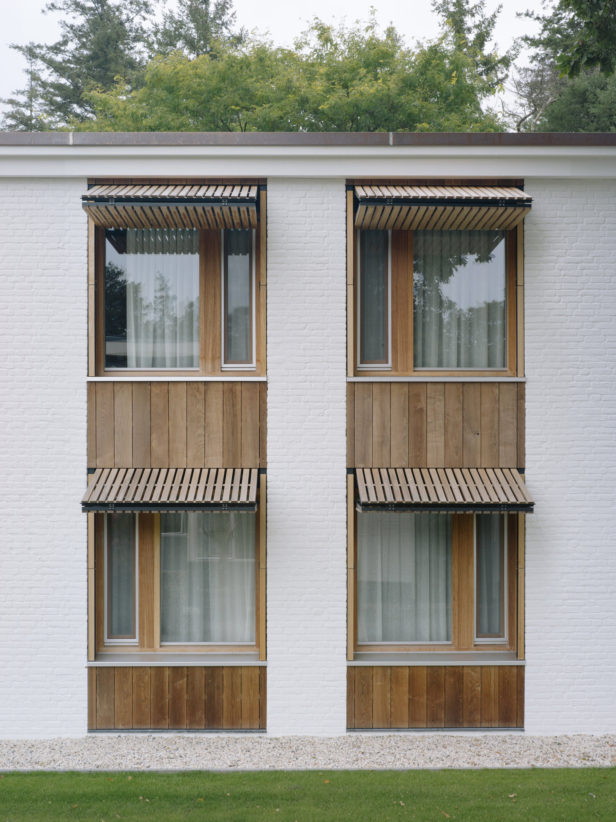 Four stacked windows with timber cladding and corrugated metal awnings on a white brick wall