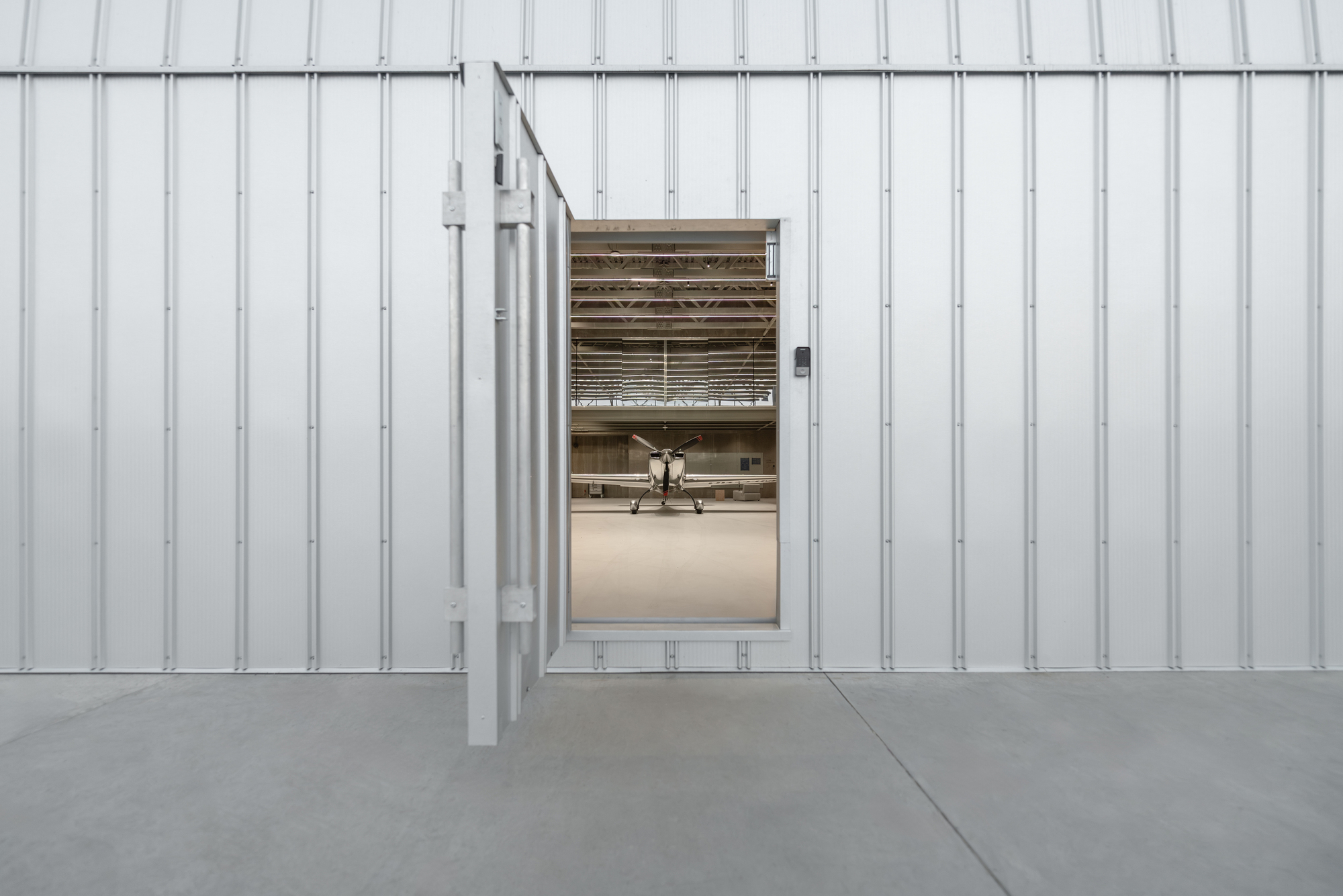 Corrugated metal cladding wall with open sliding door revealing aircraft inside the hangar bay