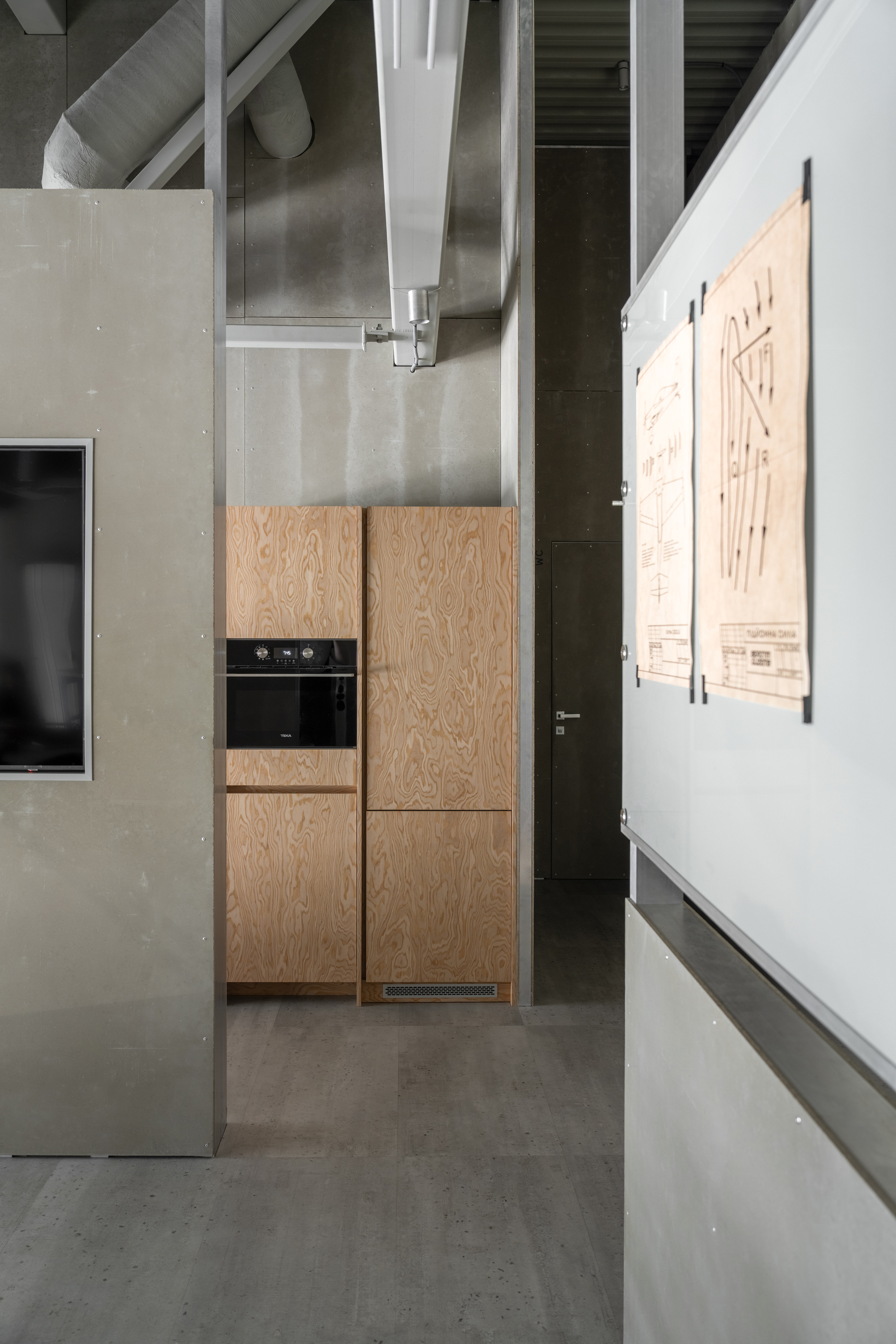 Kitchenette with pale wood veneer cabinetry, built-in oven, and exposed structural beams overhead