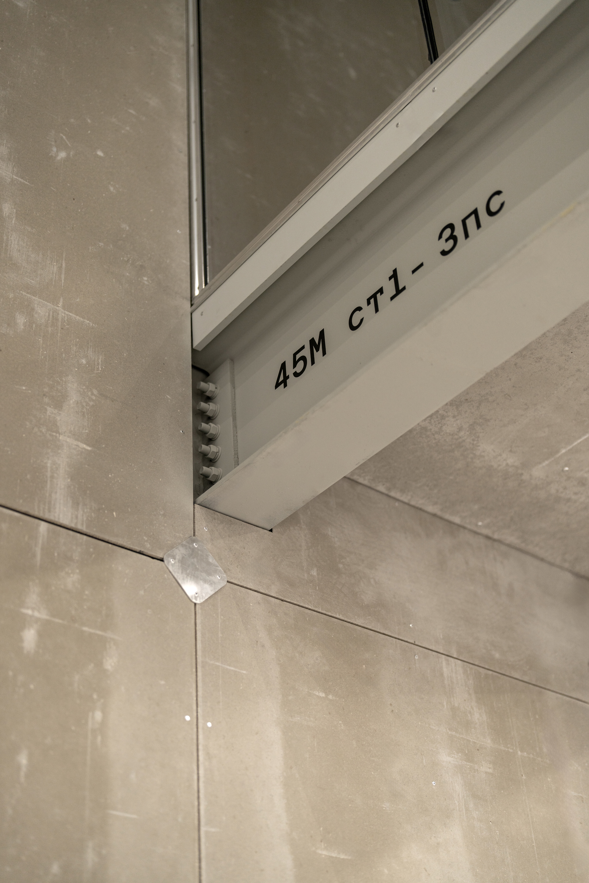 Close-up of white steel frame member with stenciled code marking against concrete panel joint