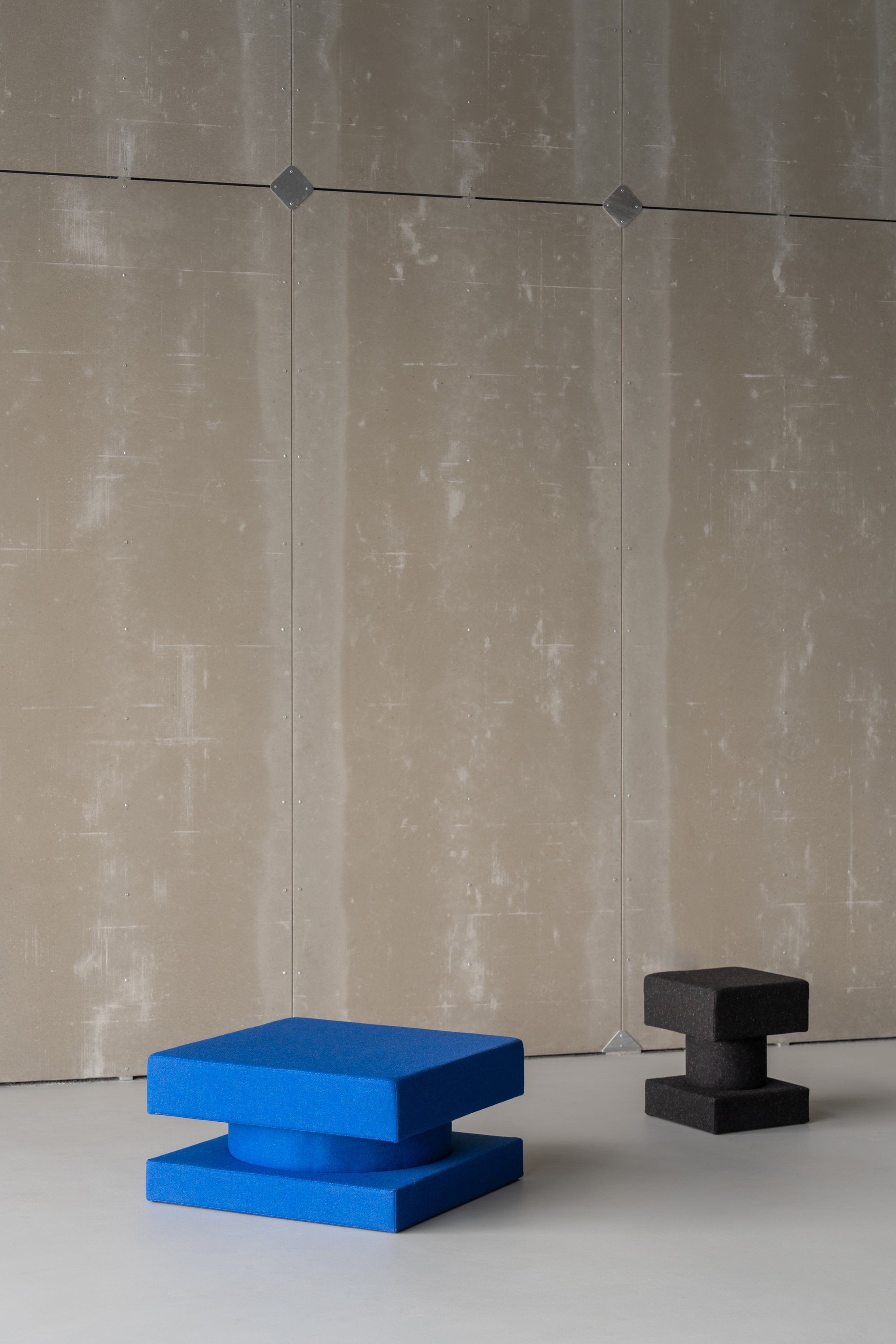 Blue and black sculptural seating blocks on a white floor against weathered concrete panel walls