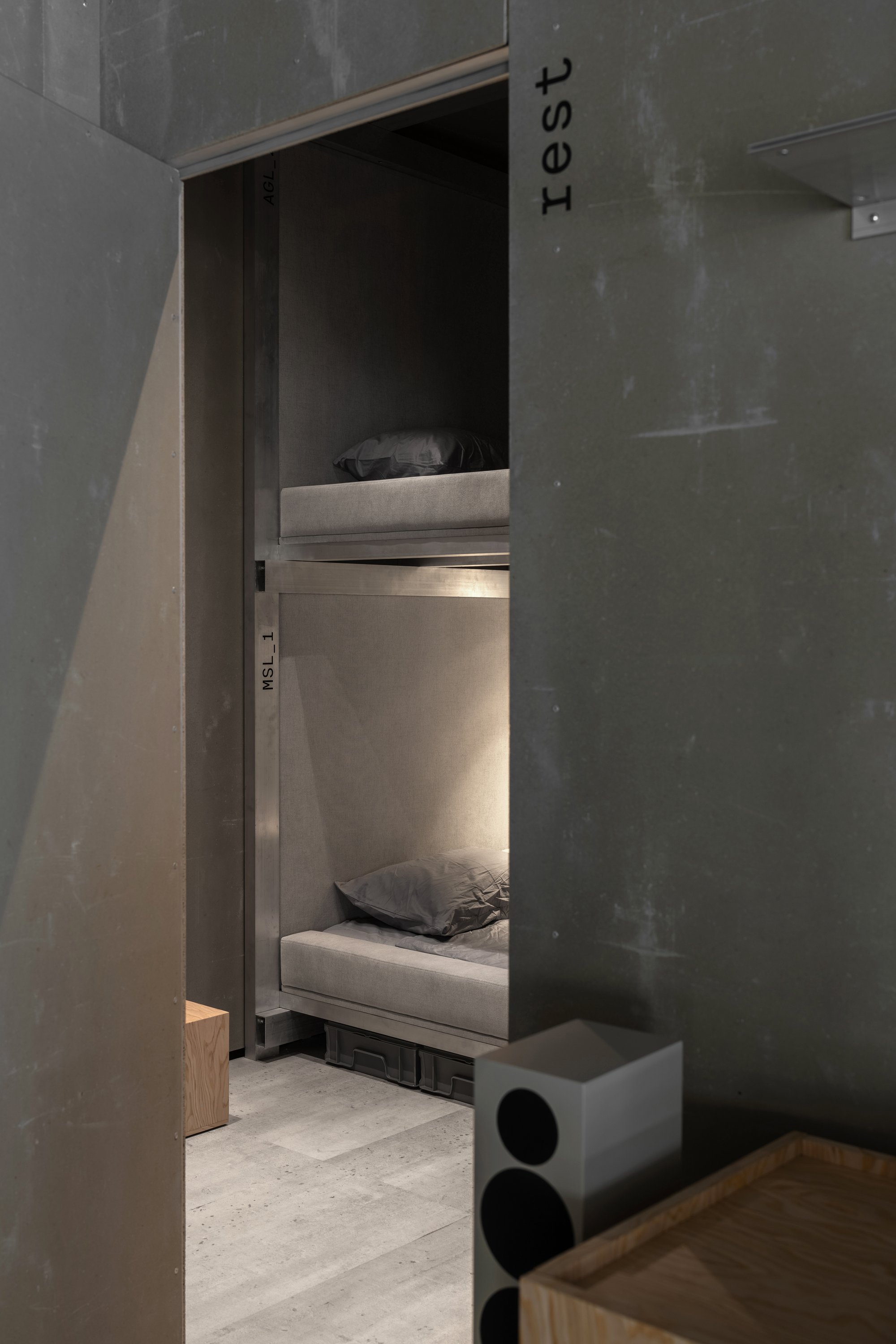 View into a sleeping alcove with stacked bunk beds and integrated lighting beside concrete walls
