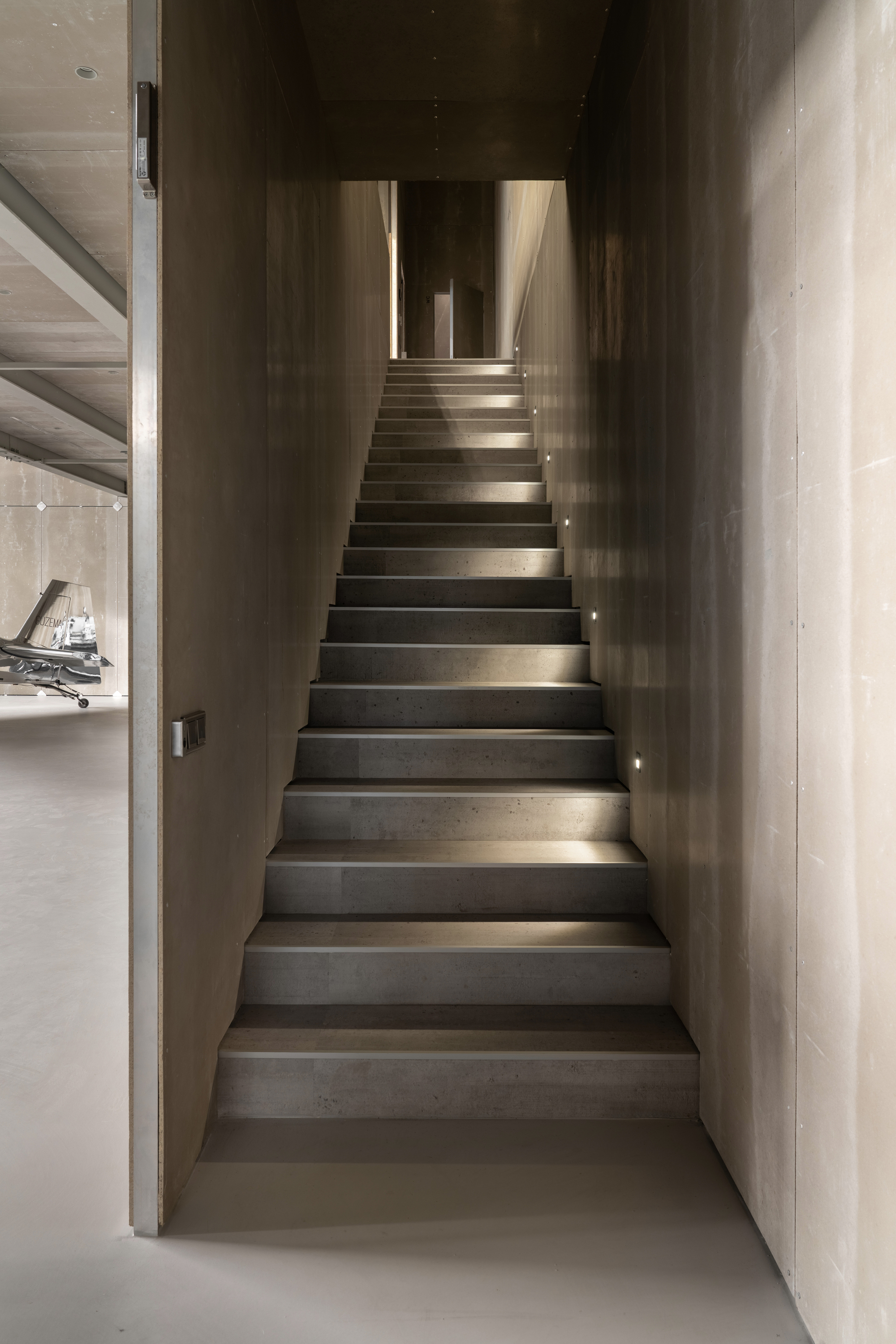 Narrow concrete stairwell with integrated step lighting ascending between dark walls