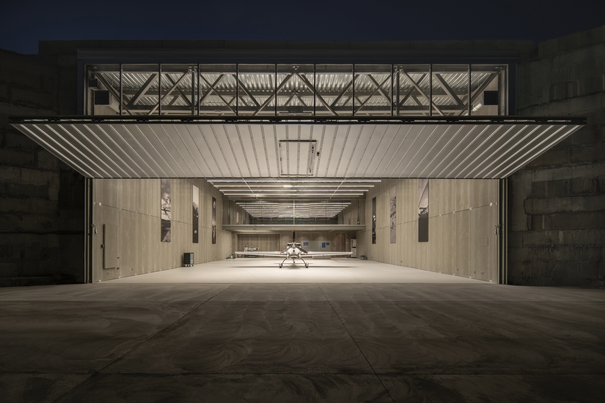 Exterior view of the open hangar door with corrugated metal soffit and exposed truss structure at dusk