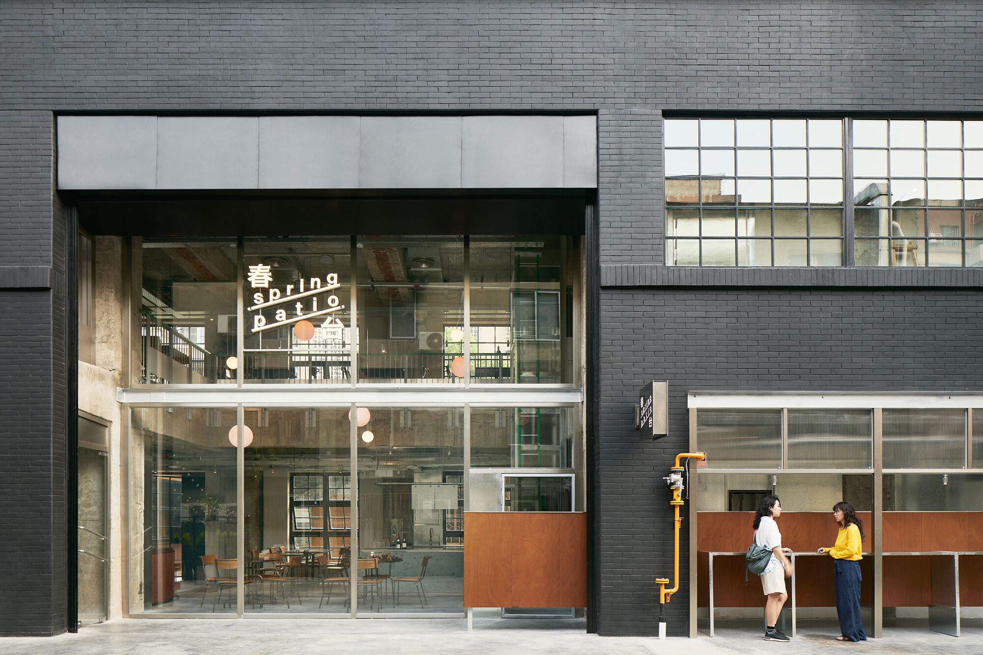 Street-level facade with dark brick cladding and double-height glazed entrance with two figures conversing