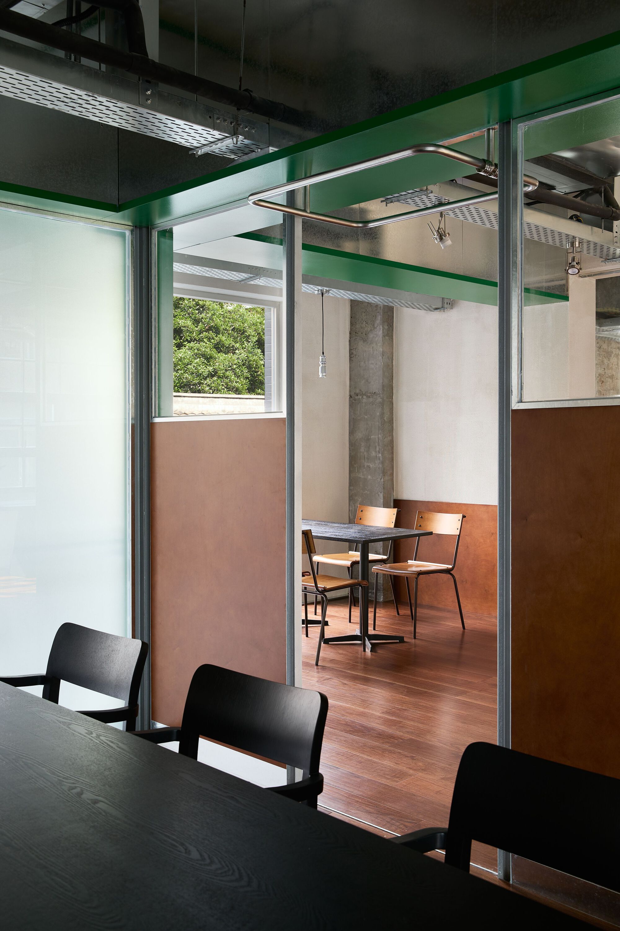 Seating booth framed by steel posts and glass partition with copper-clad lower wall panels