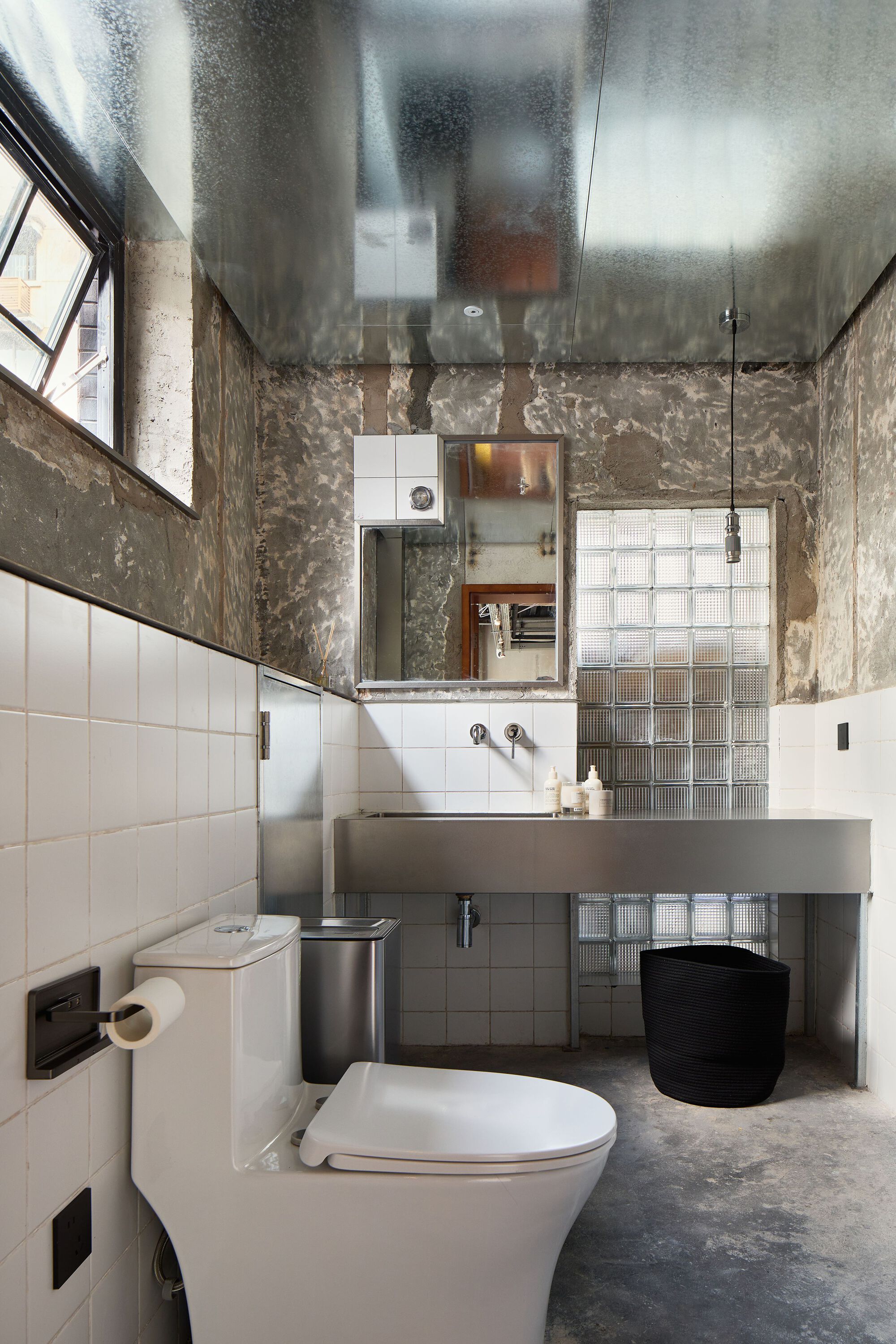 Compact bathroom with reflective metal ceiling and white tile wainscoting under textured concrete walls
