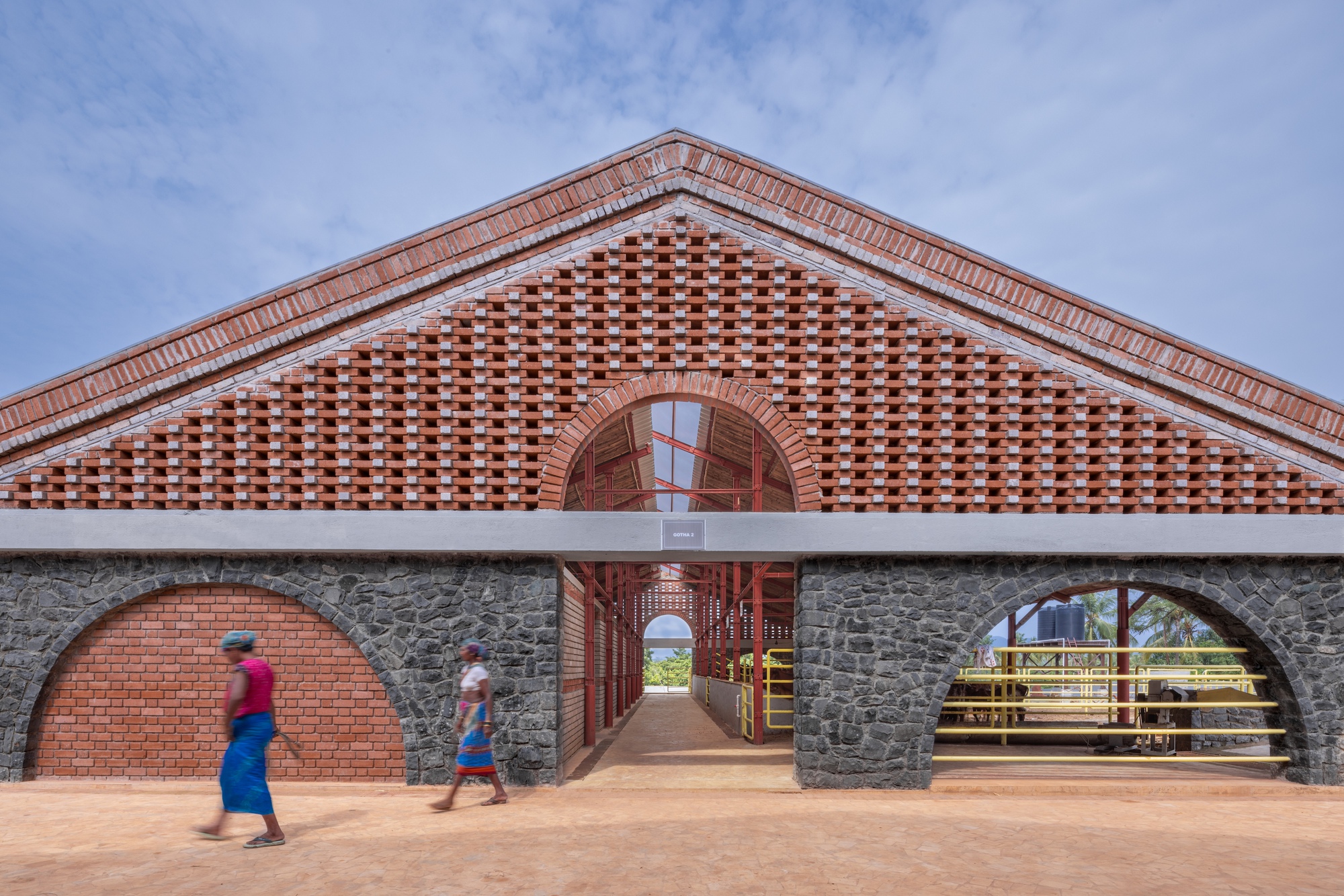 Triangular brick gable with chequered pattern above stone arches as two people walk past
