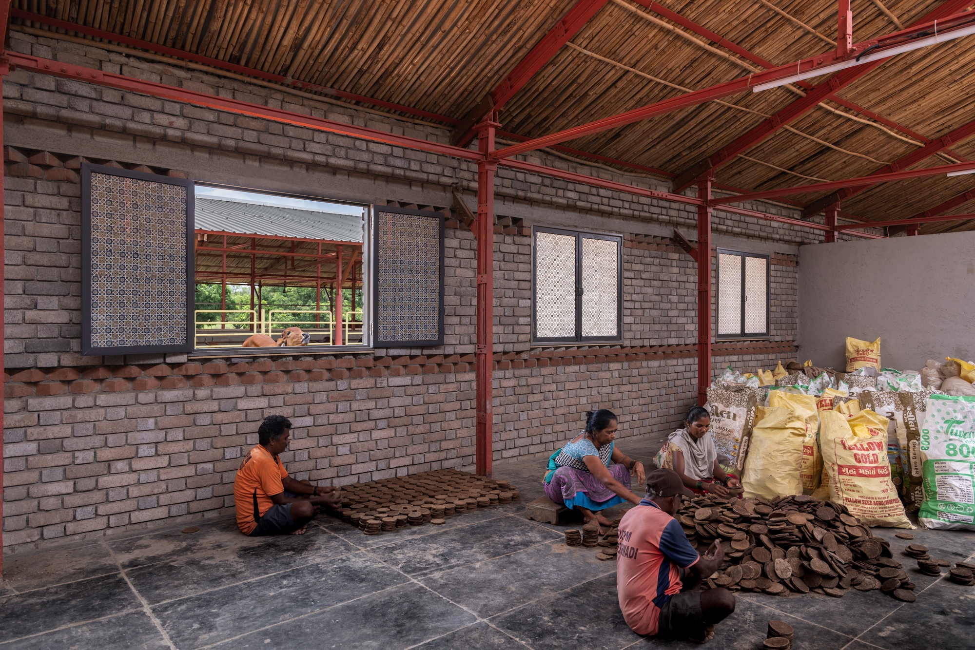 Interior space with brick walls and red steel columns where four people sit sorting materials