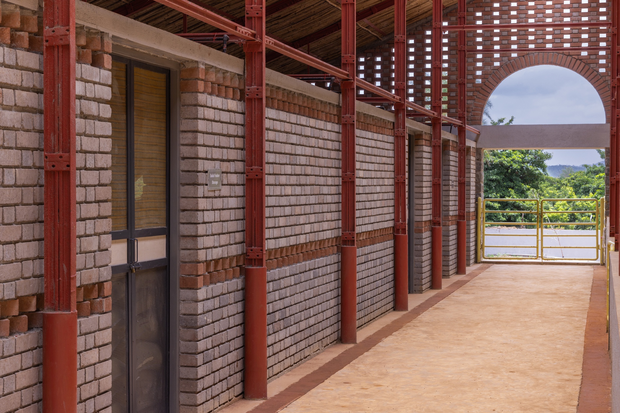 Covered walkway with red steel columns, light brick walls and exposed timber ceiling framing distant mountains