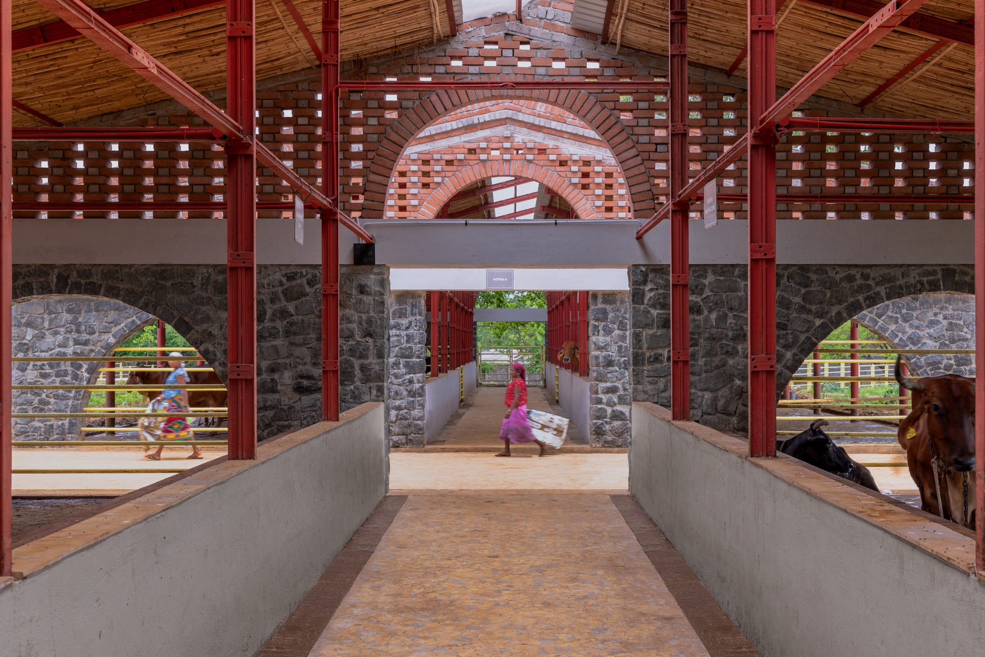 Interior passage with concrete ramp, red steel columns and brick archways framing figures and cattle outside