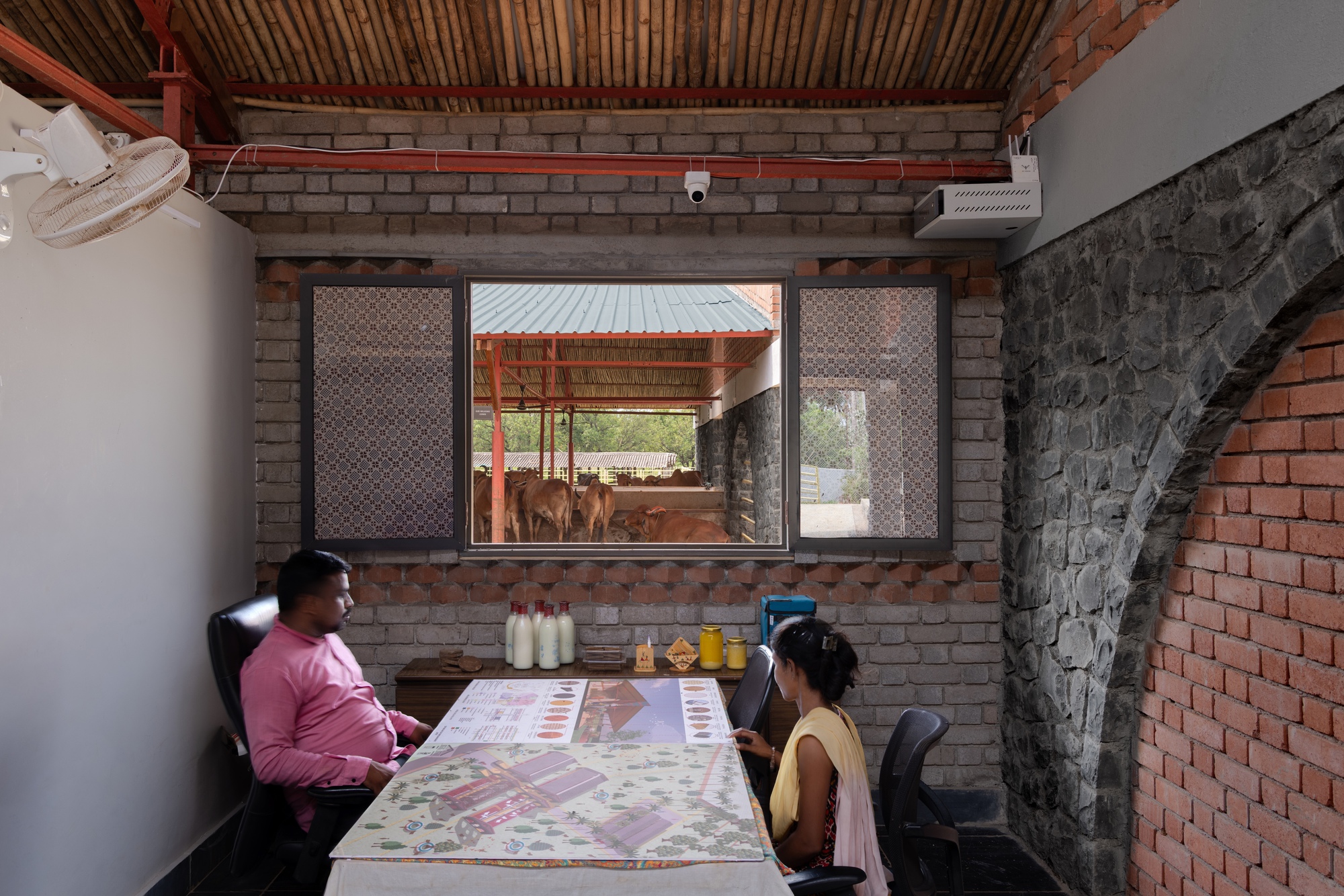 Office interior with two people at a table framed by perforated brick screens overlooking the cattle enclosure