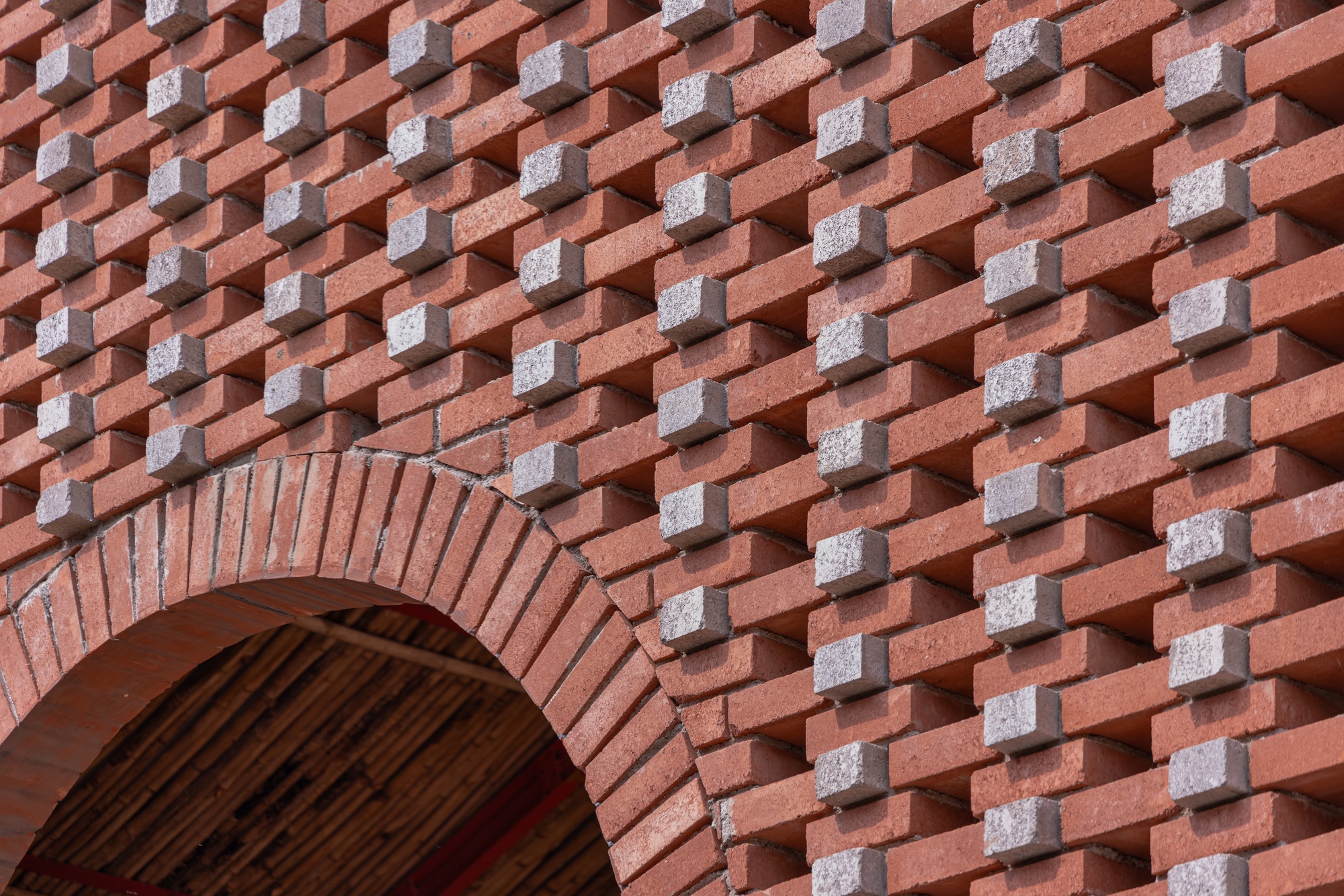 Patterned brick wall with alternating red and grey units forming a basketweave texture around an arched opening