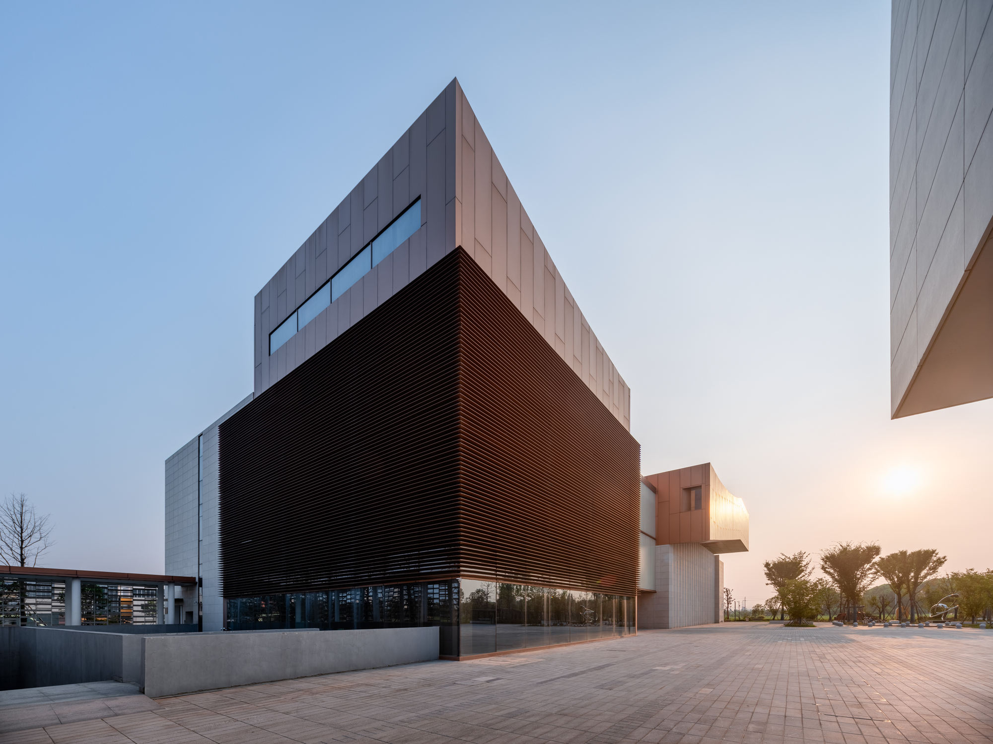 Corner view showing the horizontal bronze louver volume cantilevered above the concrete base at dusk
