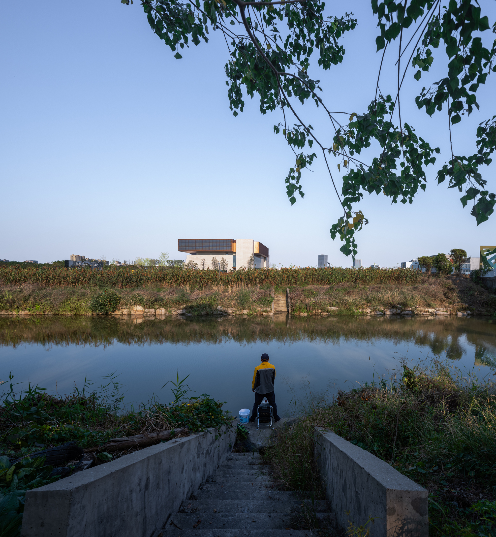 Figure on concrete steps leading to a pond with the cantilevered volume visible across the water at dusk
