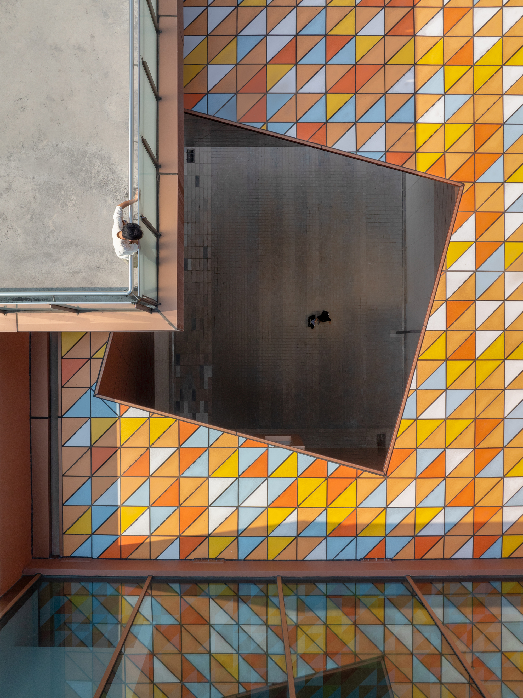 Overhead view of a central courtyard with multicolored triangular tile pavement and a person walking below