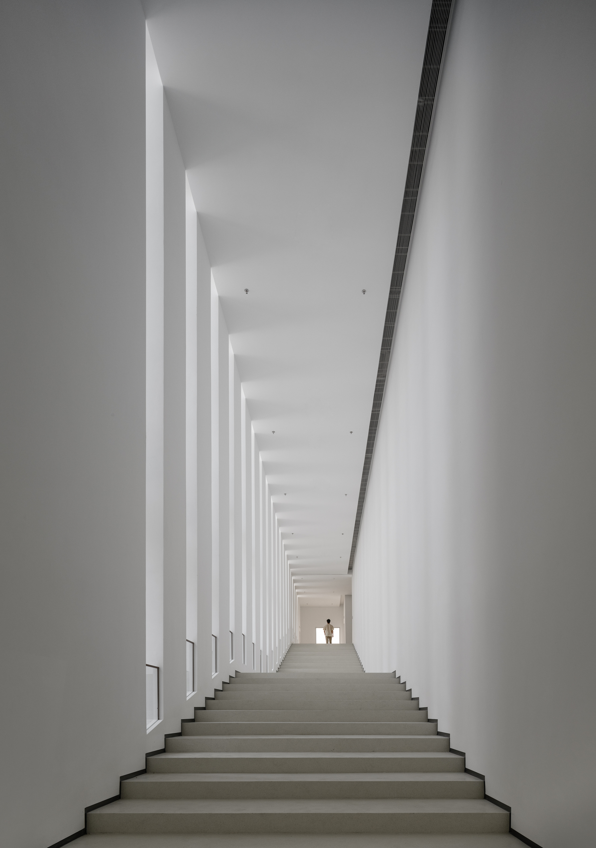 White staircase flanked by vertical columns of daylight with two figures silhouetted at the top