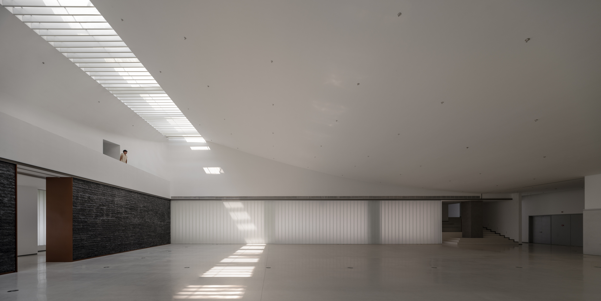 Gallery interior with linear skylight casting sharp shadows across the polished concrete floor
