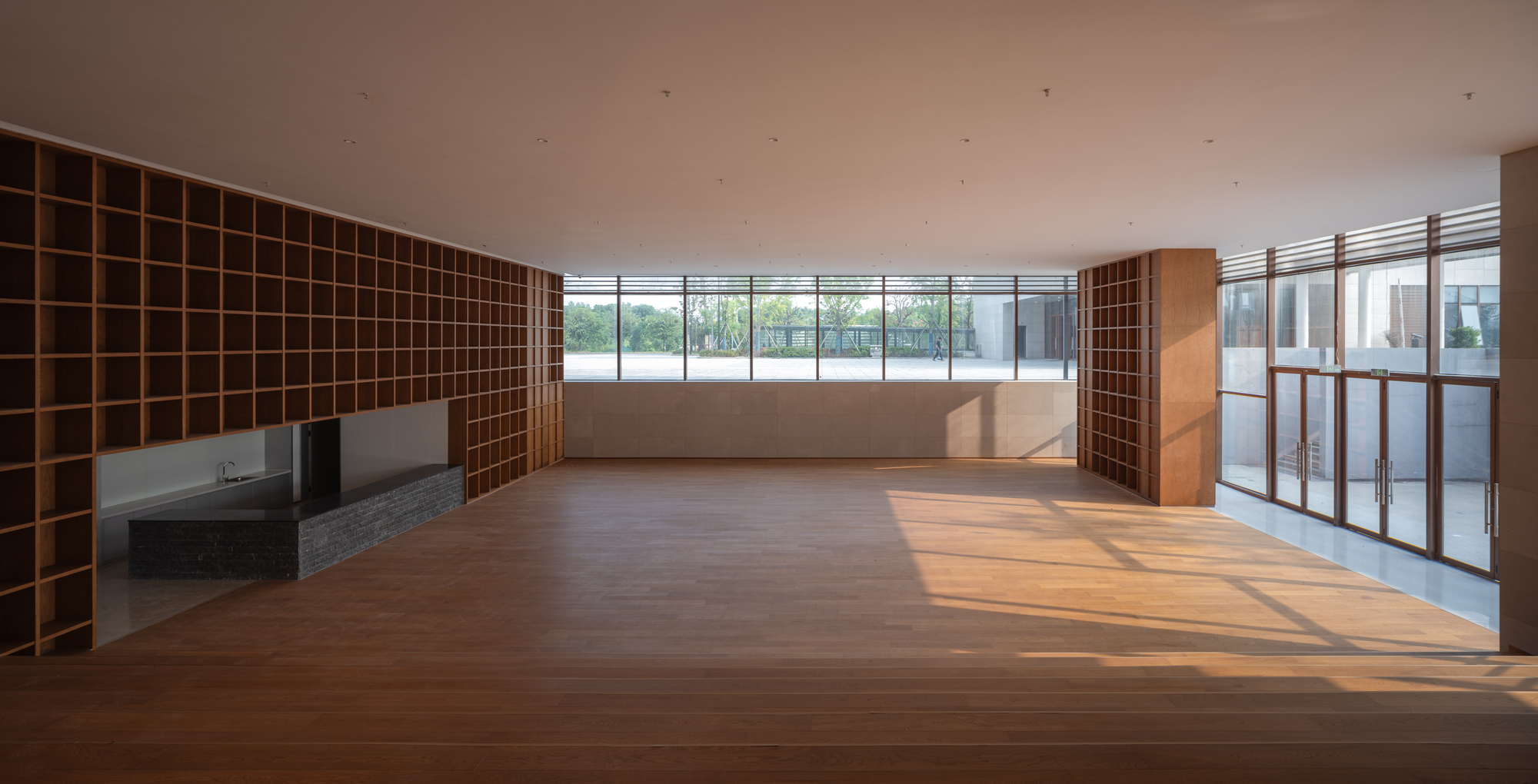 Open-plan interior with timber shelving grid, stone floor and ribbon windows overlooking a terrace