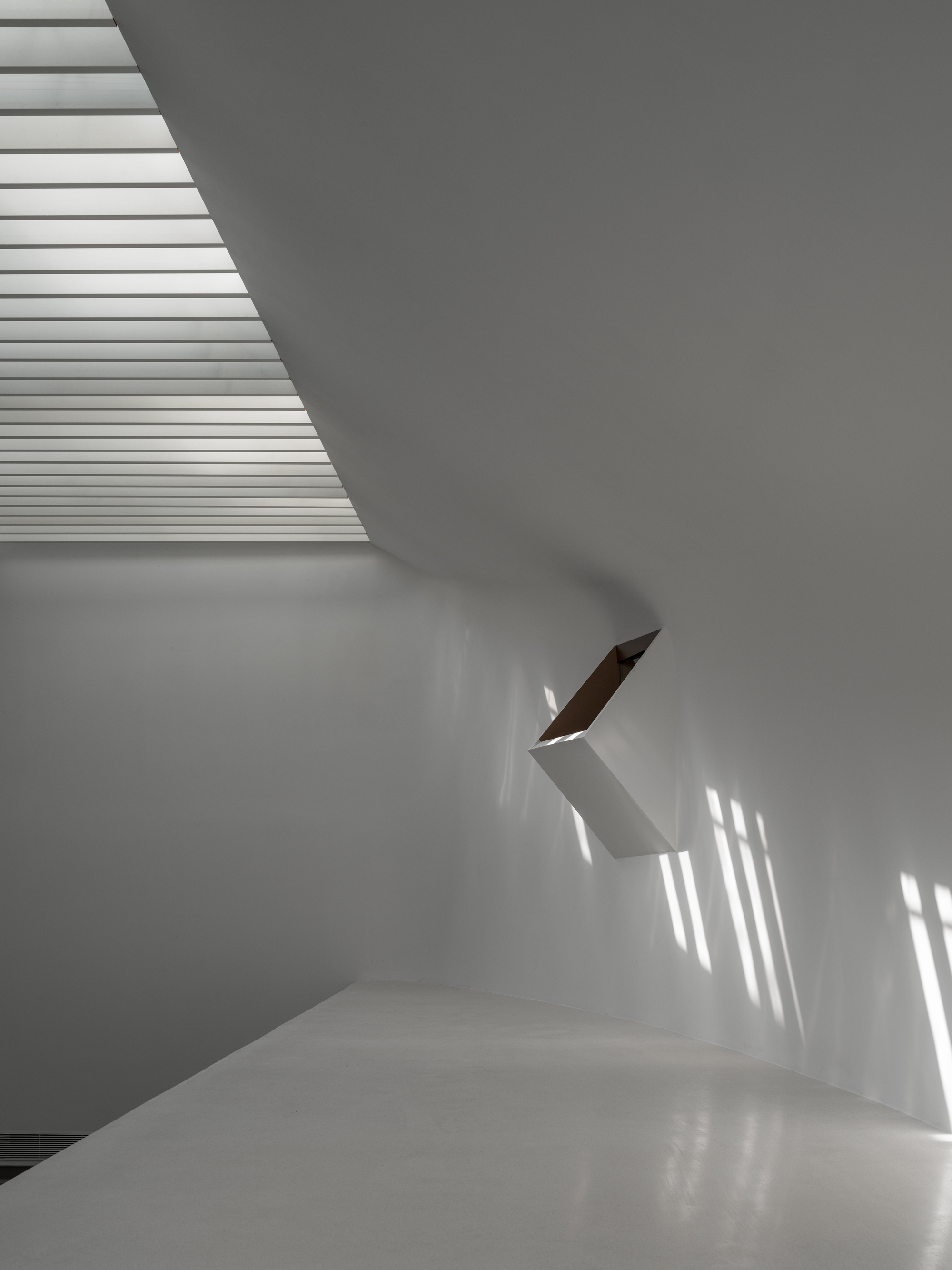 White interior staircase with timber handrail catching striped shadows from overhead louvers