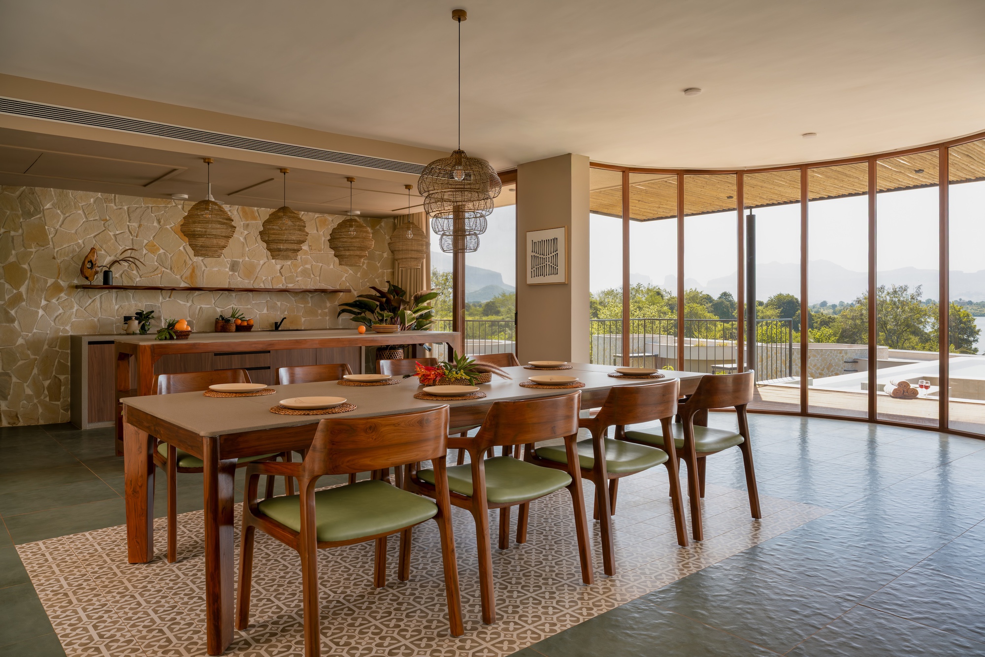Dining room with timber table, woven pendant lights and full-height curved glass wall overlooking distant hills