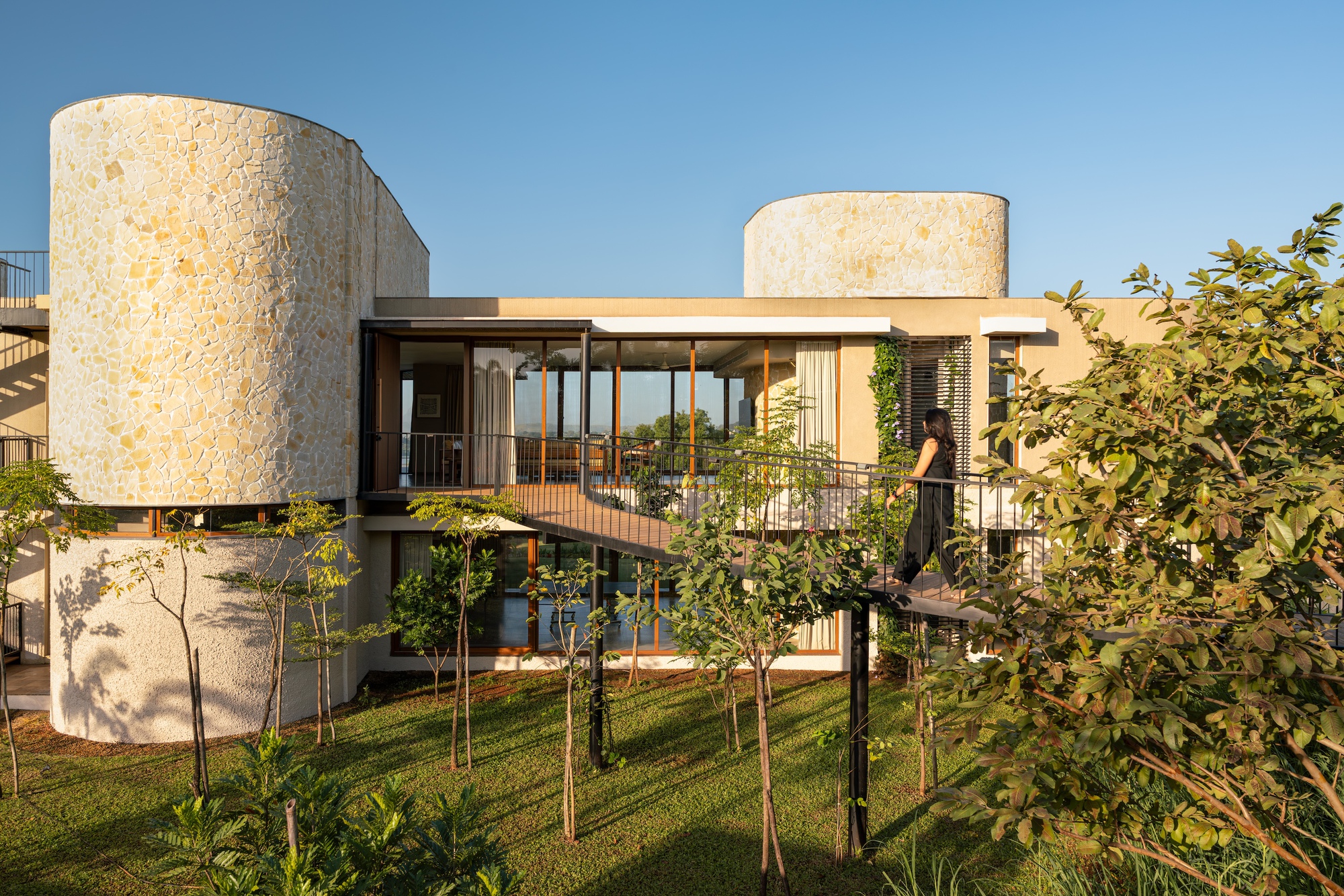 Two-level facade with stone cylindrical towers, timber-framed glazing, and metal balustrades overlooking a lawn