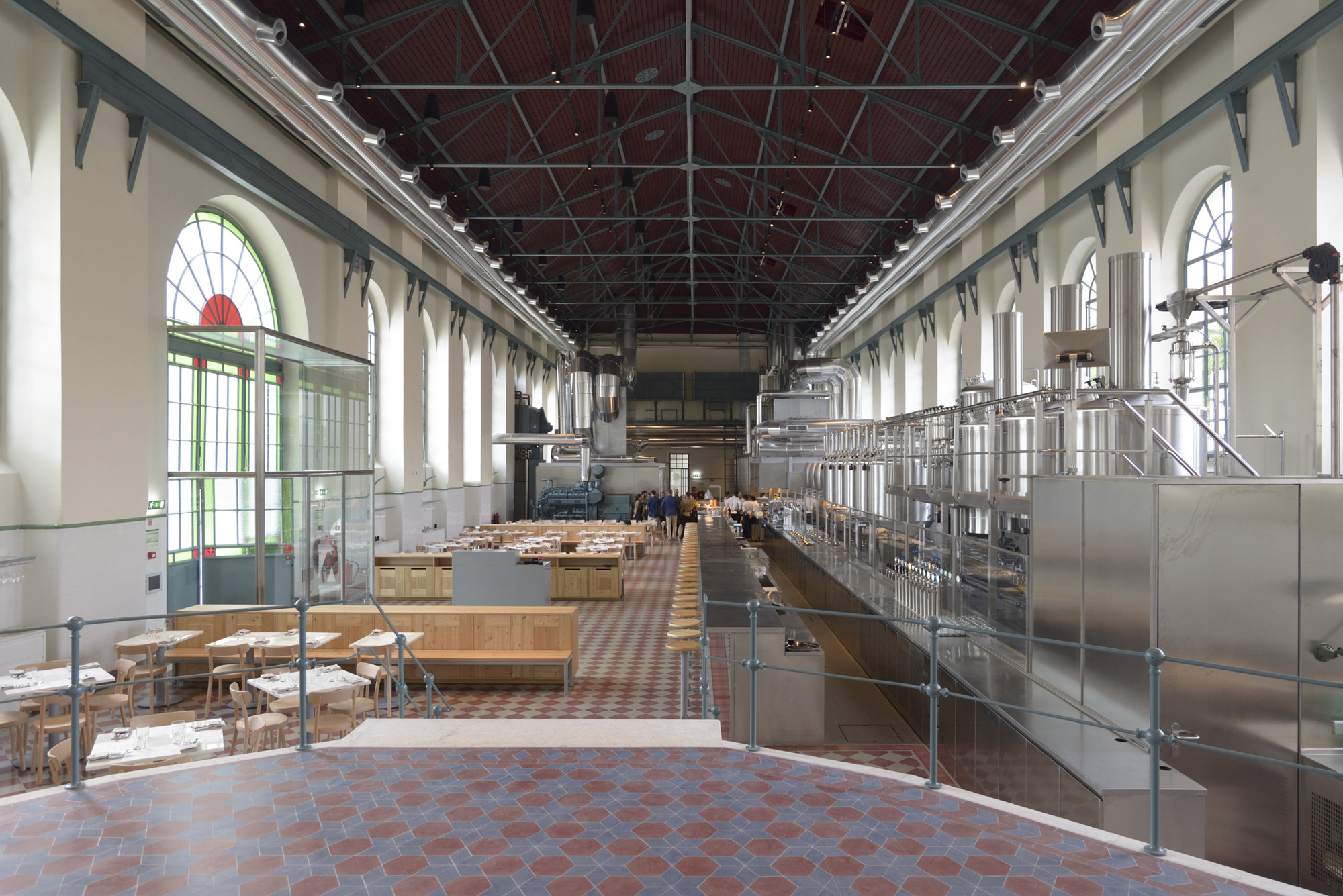 Interior hall with stainless steel brewing equipment along one side and arched windows flooding the terracotta floor