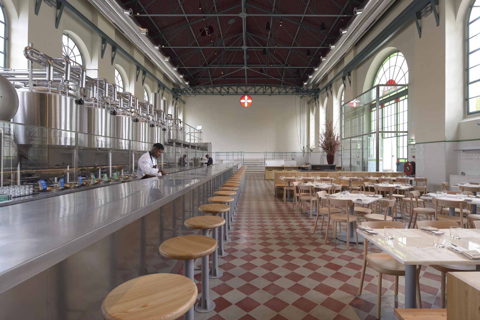 Long counter with circular stools facing stainless steel equipment under an exposed truss ceiling with red tiles