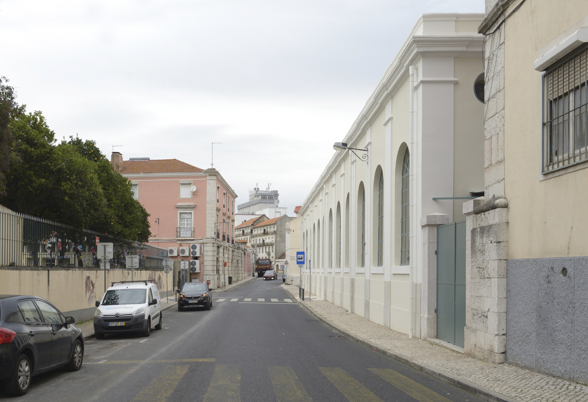 Street view of a white rendered facade with arched openings and parked cars along the road