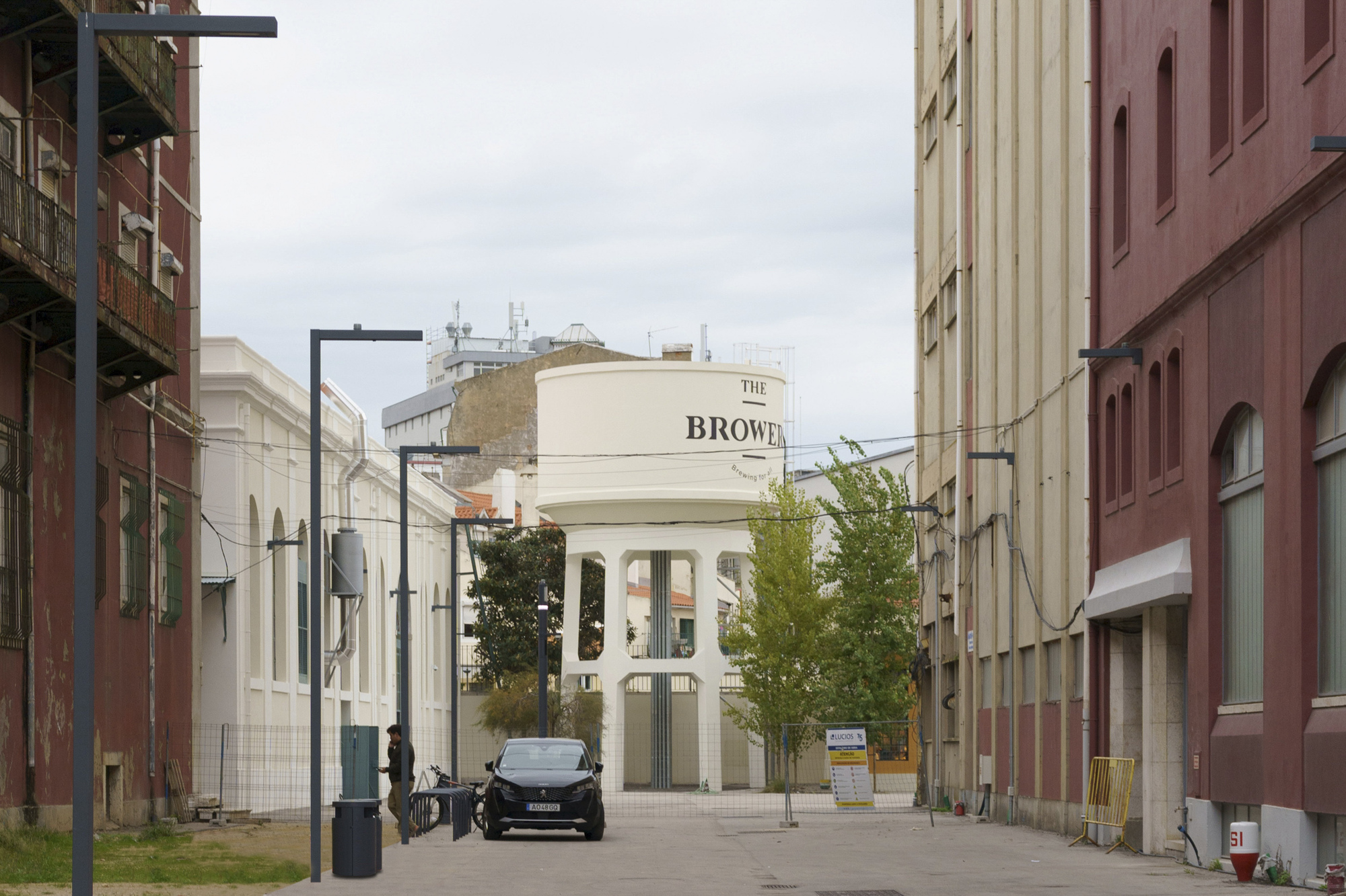 Pedestrian plaza framed by industrial buildings with a cylindrical water tower in the distance