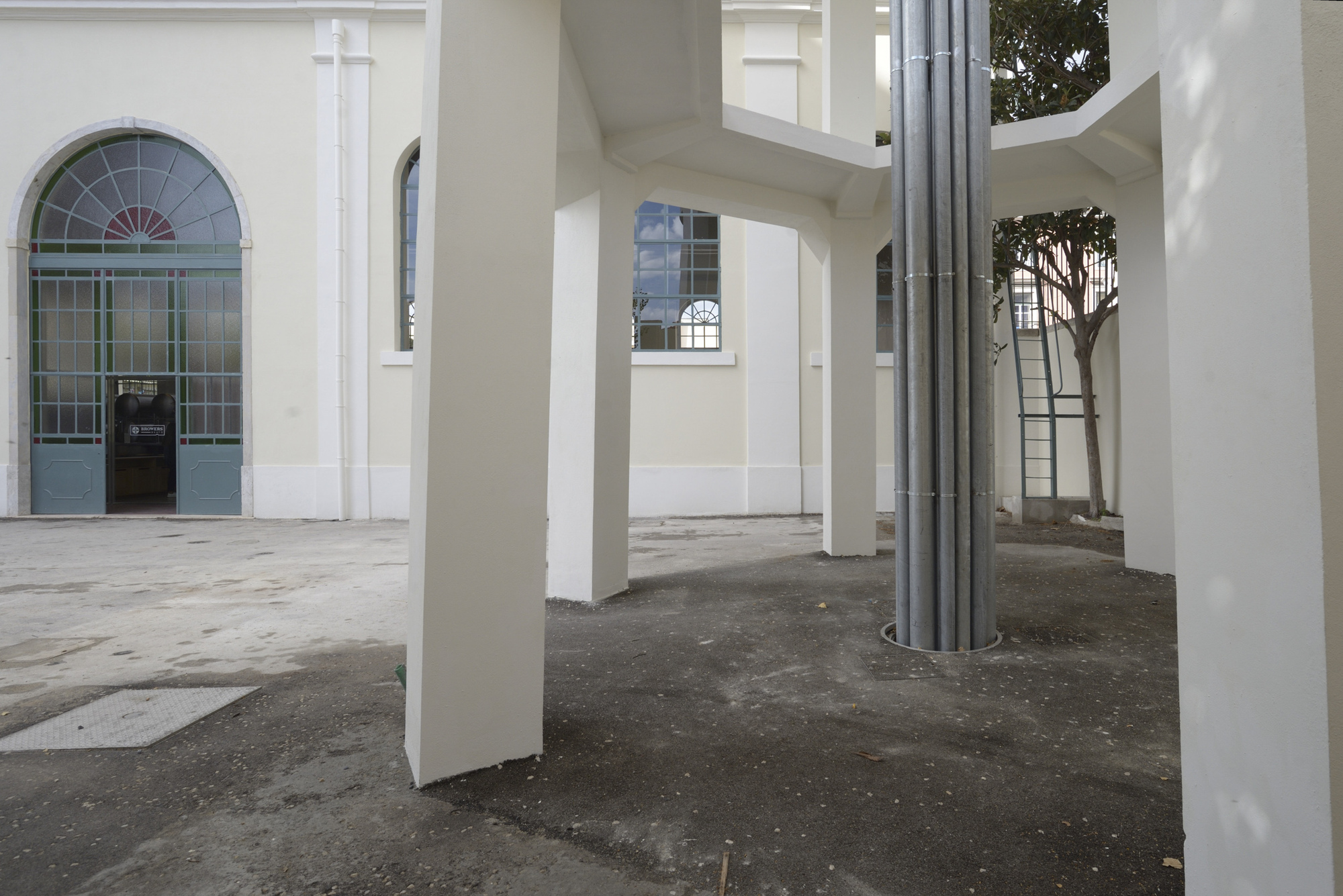 Covered arcade with white square columns and a circular metal duct wrapping around one pillar