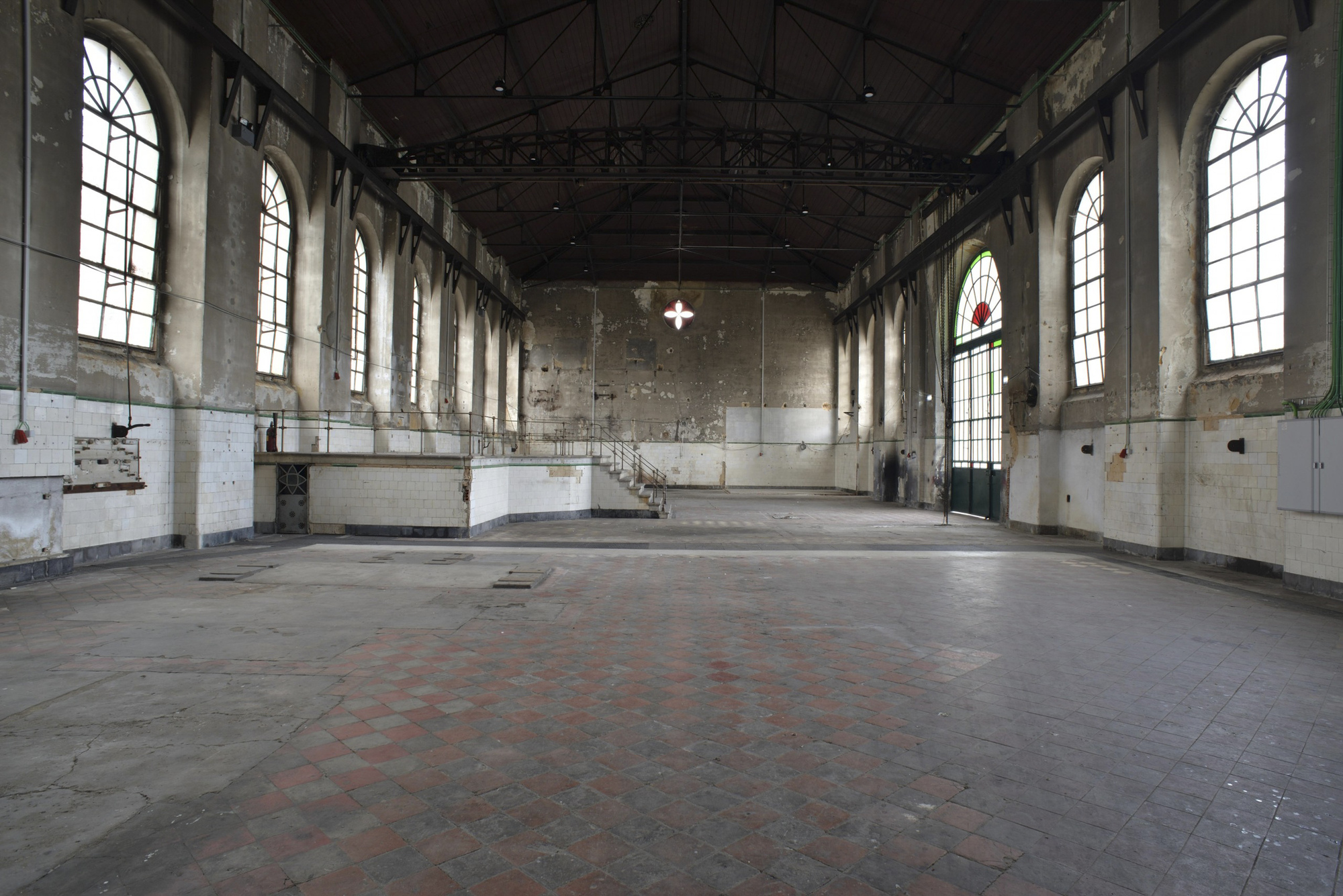 Empty interior hall with exposed concrete walls and arched windows before renovation
