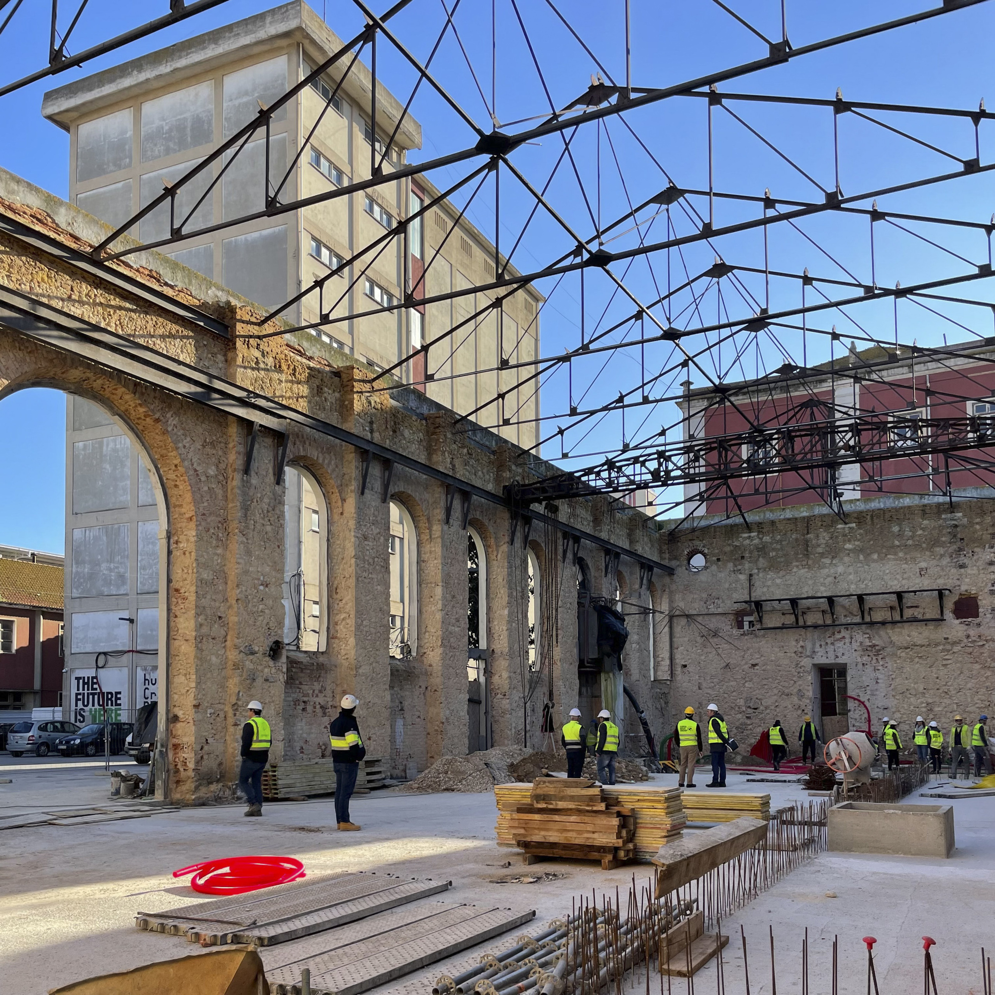 Arched stone facade beneath a new steel truss roof during construction with workers in high-visibility vests
