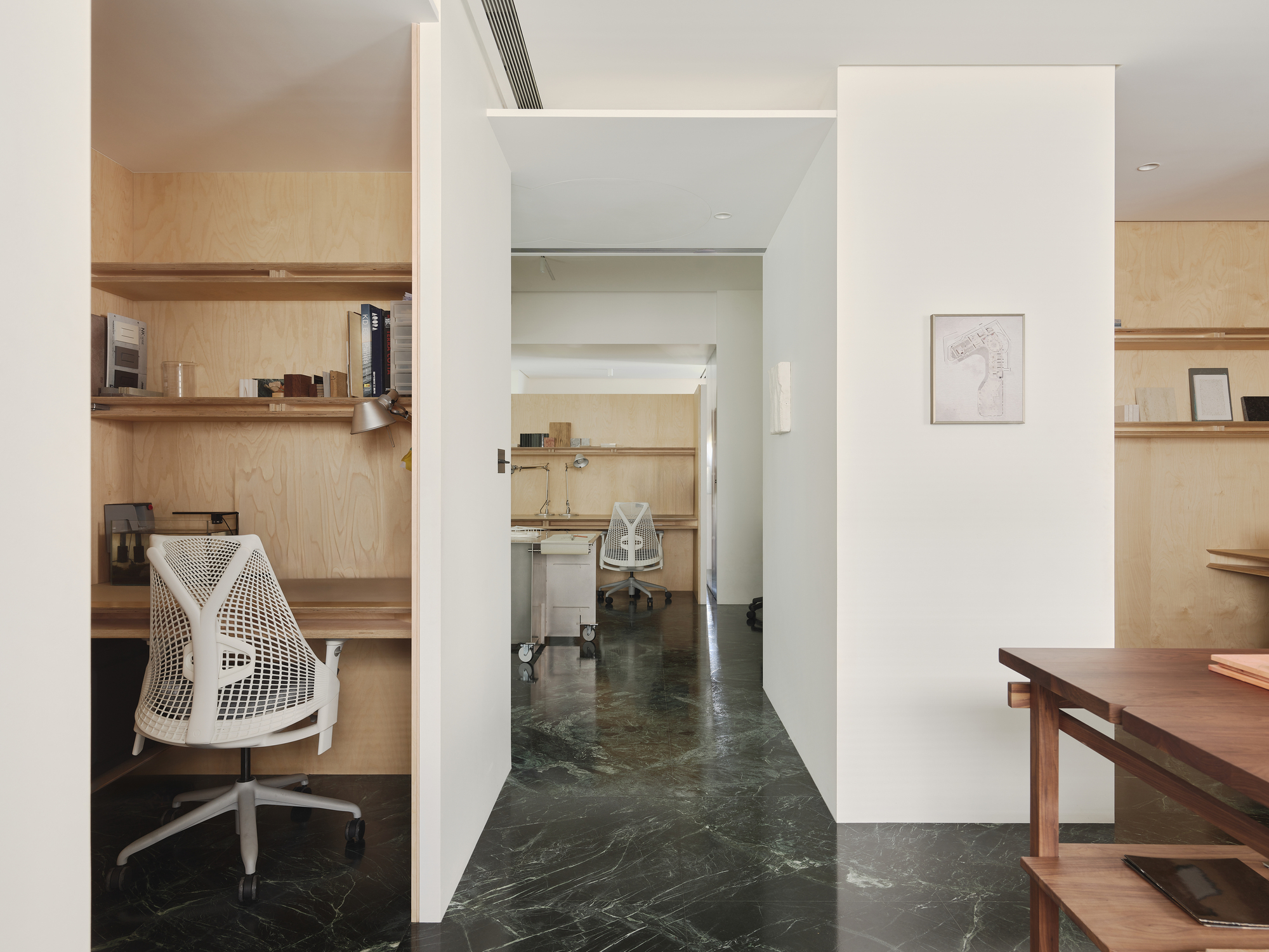 This architectural photograph showcases a modern interior with a minimalist aesthetic. The design features a compact office space with plywood shelving and a bu