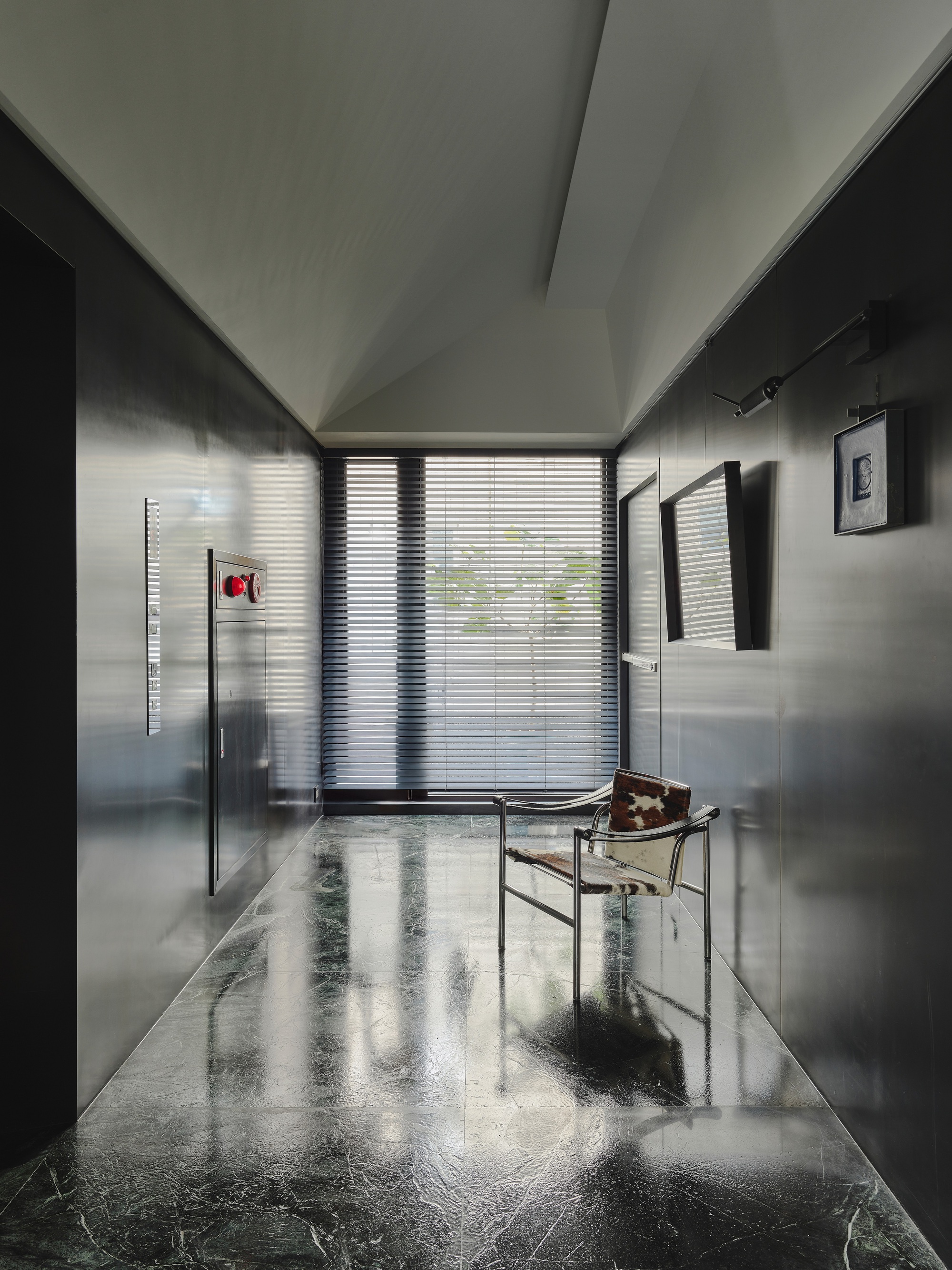 This architectural image showcases a modern hallway with a minimalist design. The space features polished marble floors, metal paneling, and a geometric ceiling