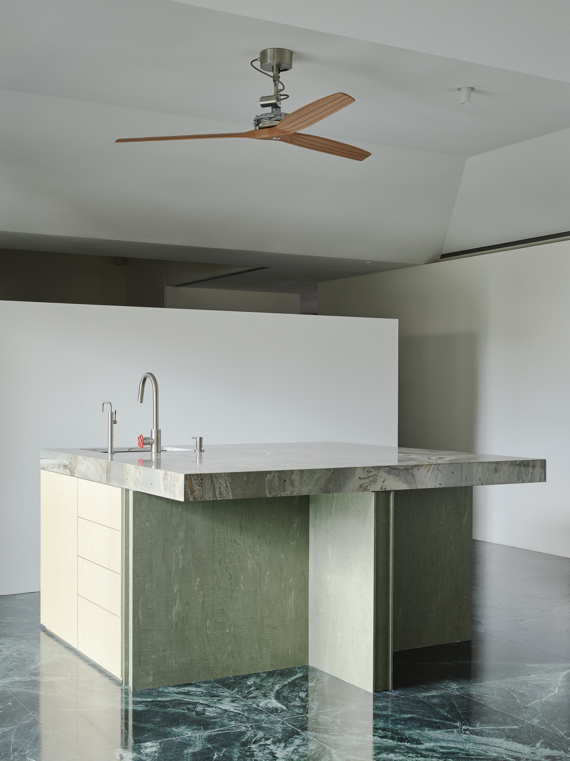 This architectural image showcases a modern kitchen island with a stone countertop and wood cabinetry, set against a marble floor. The design emphasizes clean l