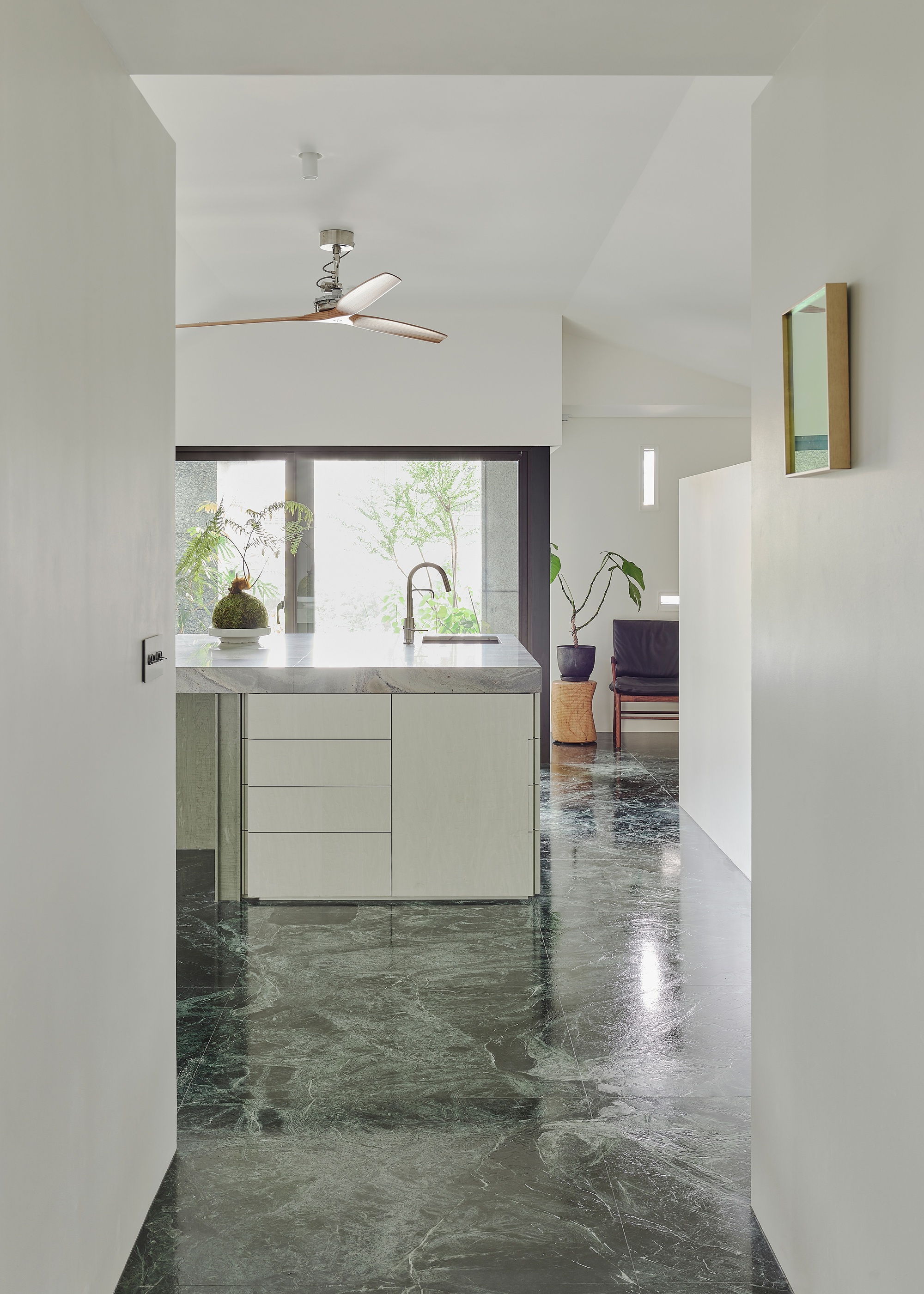 This architectural photo showcases a modern kitchen interior with a minimalist design. The space features a marble floor, a kitchen island with a marble counter