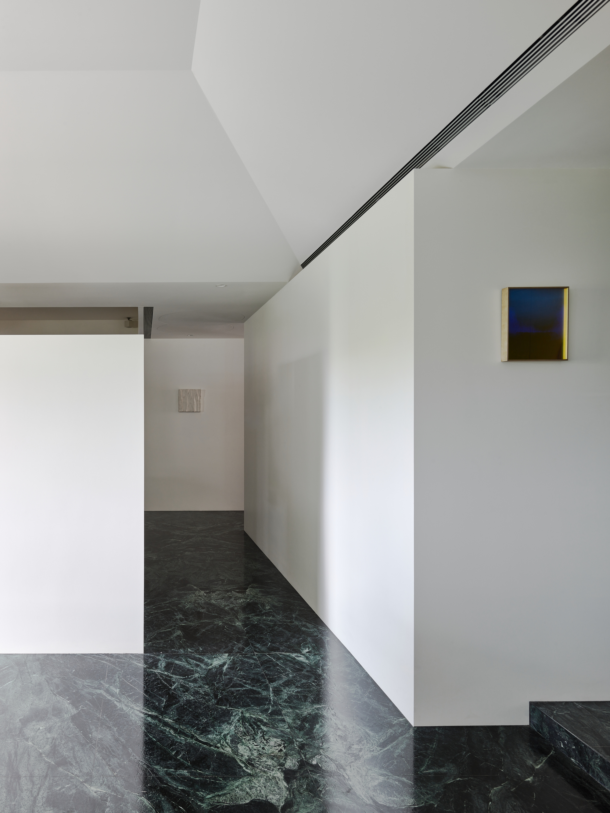 This architectural image showcases a minimalist hallway with white walls and a striking green marble floor. The space features clean lines, recessed lighting, a