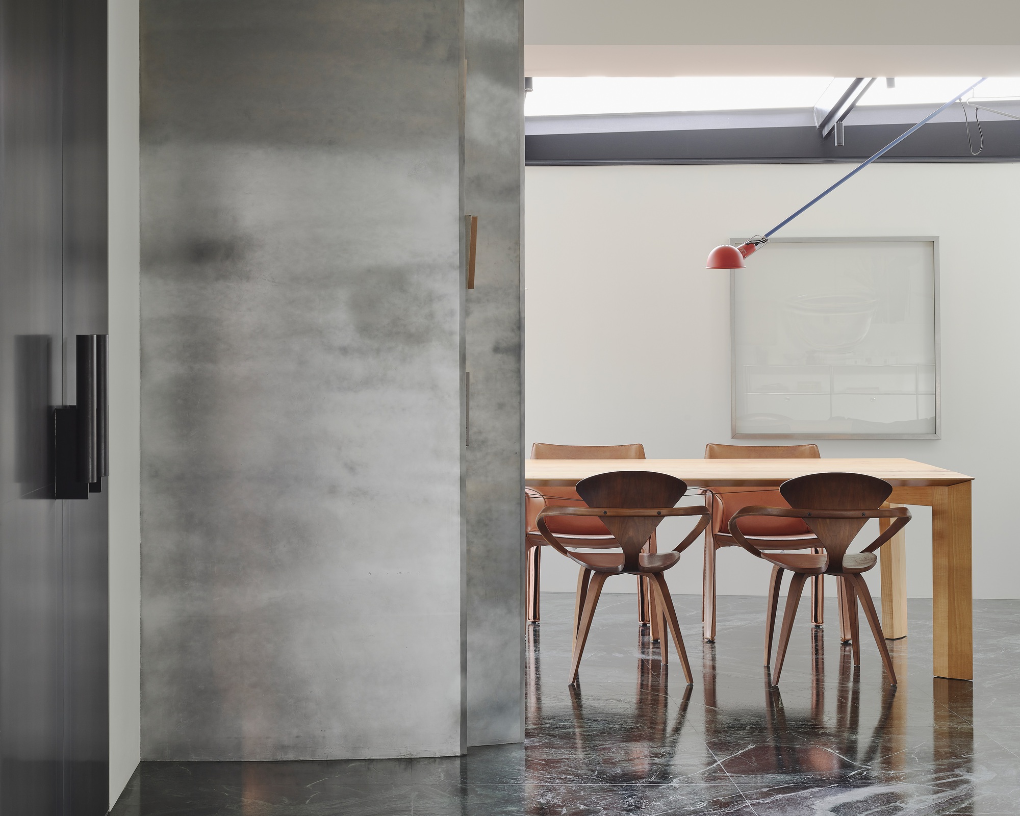 This architectural image showcases a modern dining room with a minimalist aesthetic. The space features a concrete wall with a sliding door, wooden chairs aroun