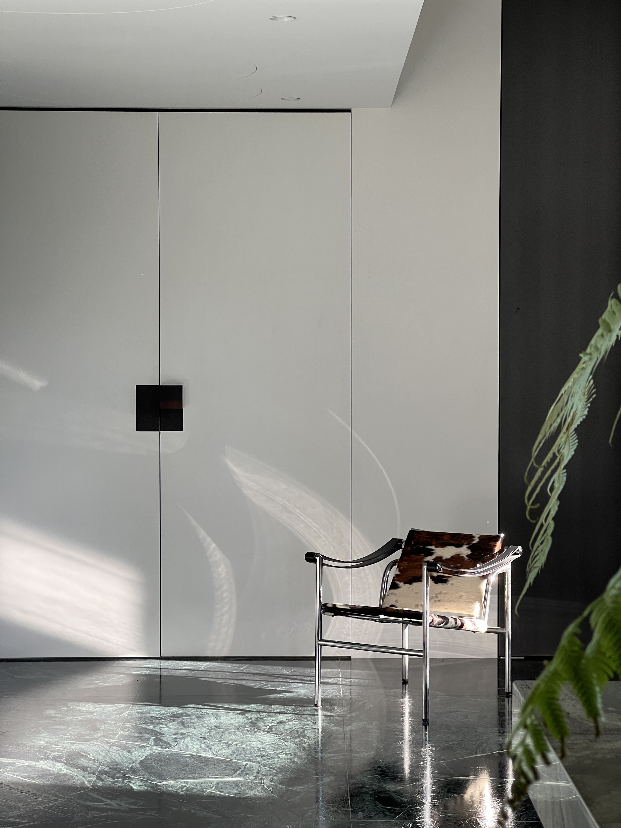 This architectural image showcases a modern interior with minimalist design elements. A chrome and cowhide chair sits against a backdrop of white walls and a bl