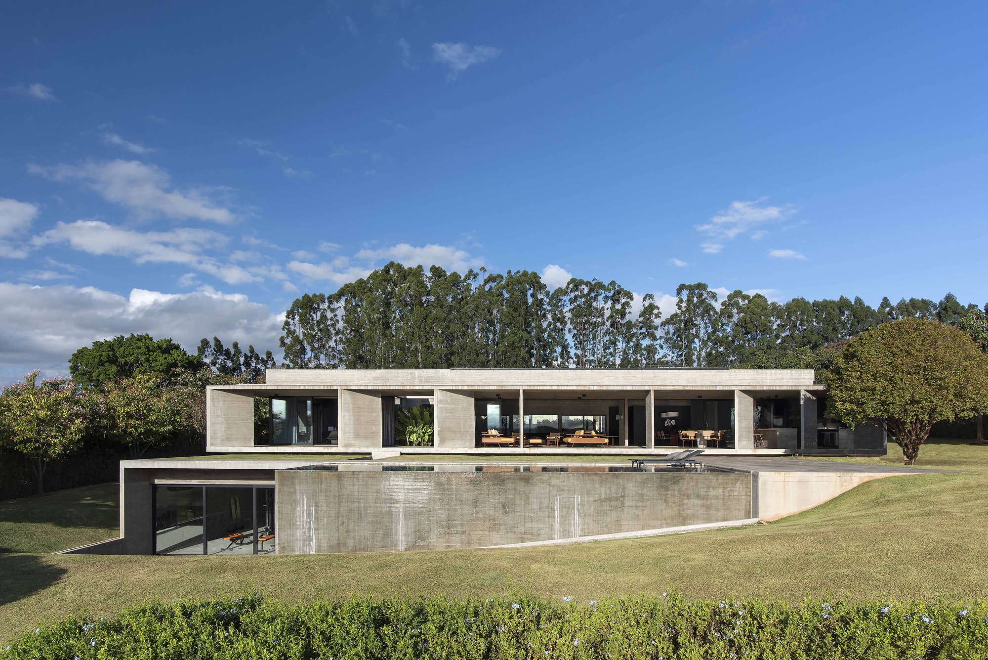 Horizontal concrete residence overlooking a lawn with eucalyptus trees under a partly cloudy sky