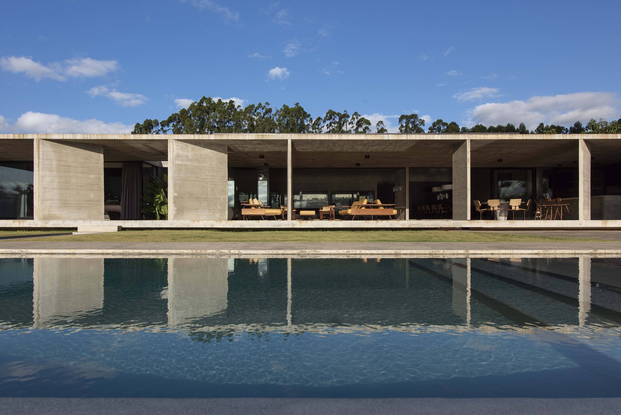 Boardmarked concrete colonnade reflected in a swimming pool with the terrace in full sun